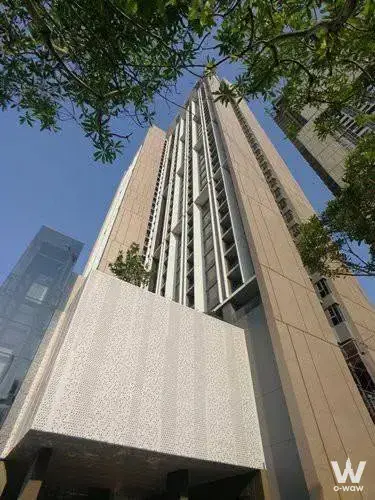 Beige stone facade of Whizdom Inspire Sukhumvit with vertical fins and a perforated entrance canopy