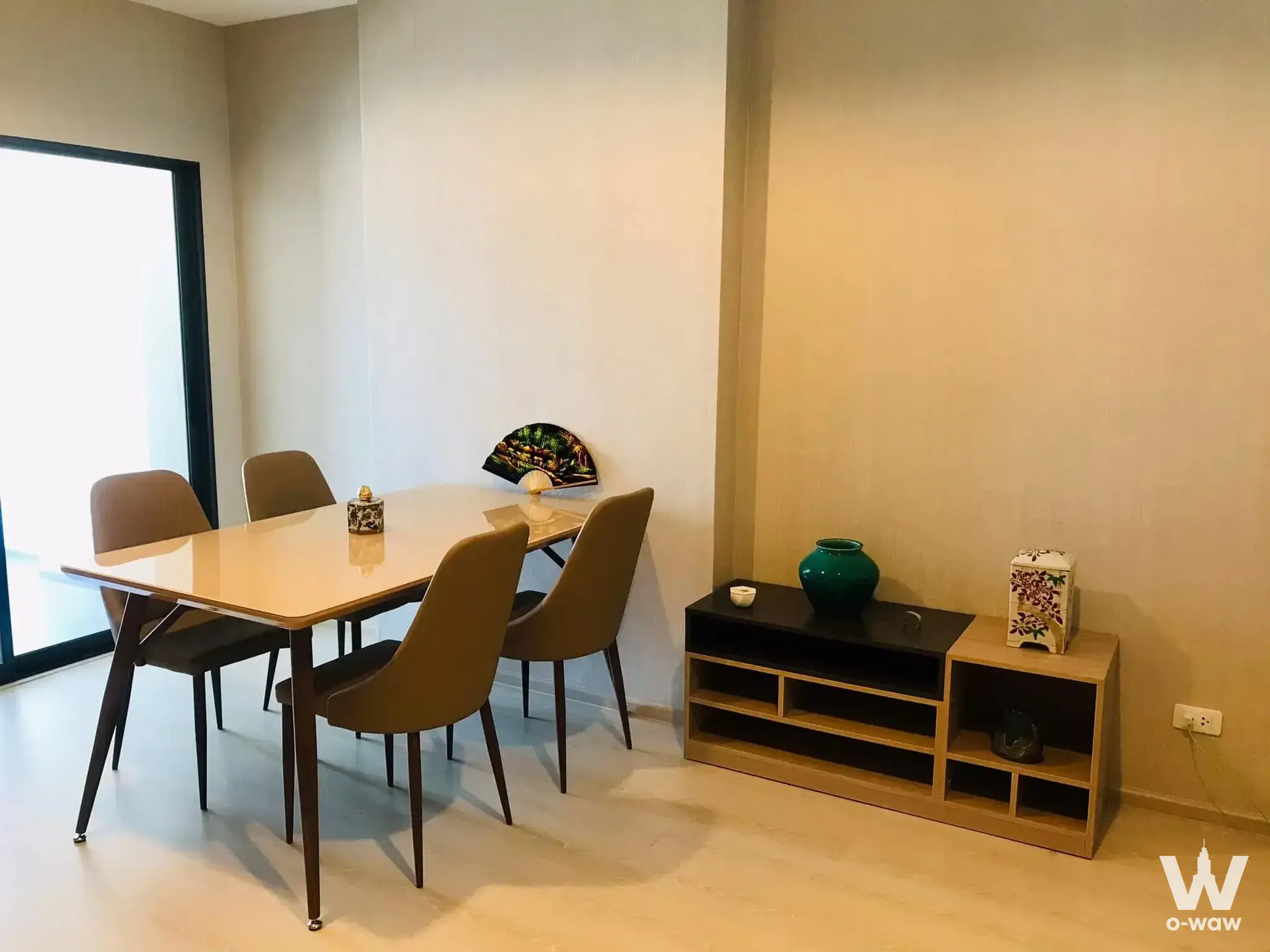 Minimalist dining area in IDEO Sukhumvit 115 condo with beige glossy table, tan chairs, and natural light from sliding door