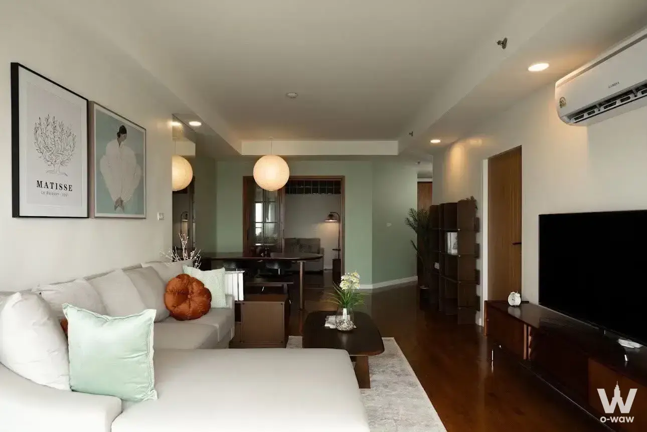 Open-plan living area in a Baan Nonzee 2-bed condo shows grey sectional and sage green accent wall