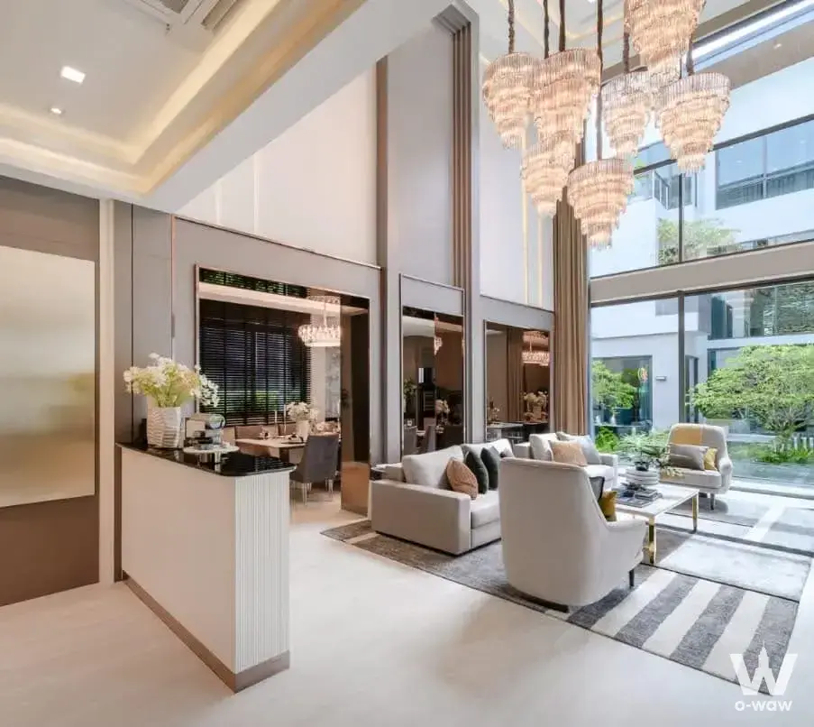 The double-height living room in a 4-bed house for sale at The Gentry Kaset has cream seating and floor-to-ceiling windows