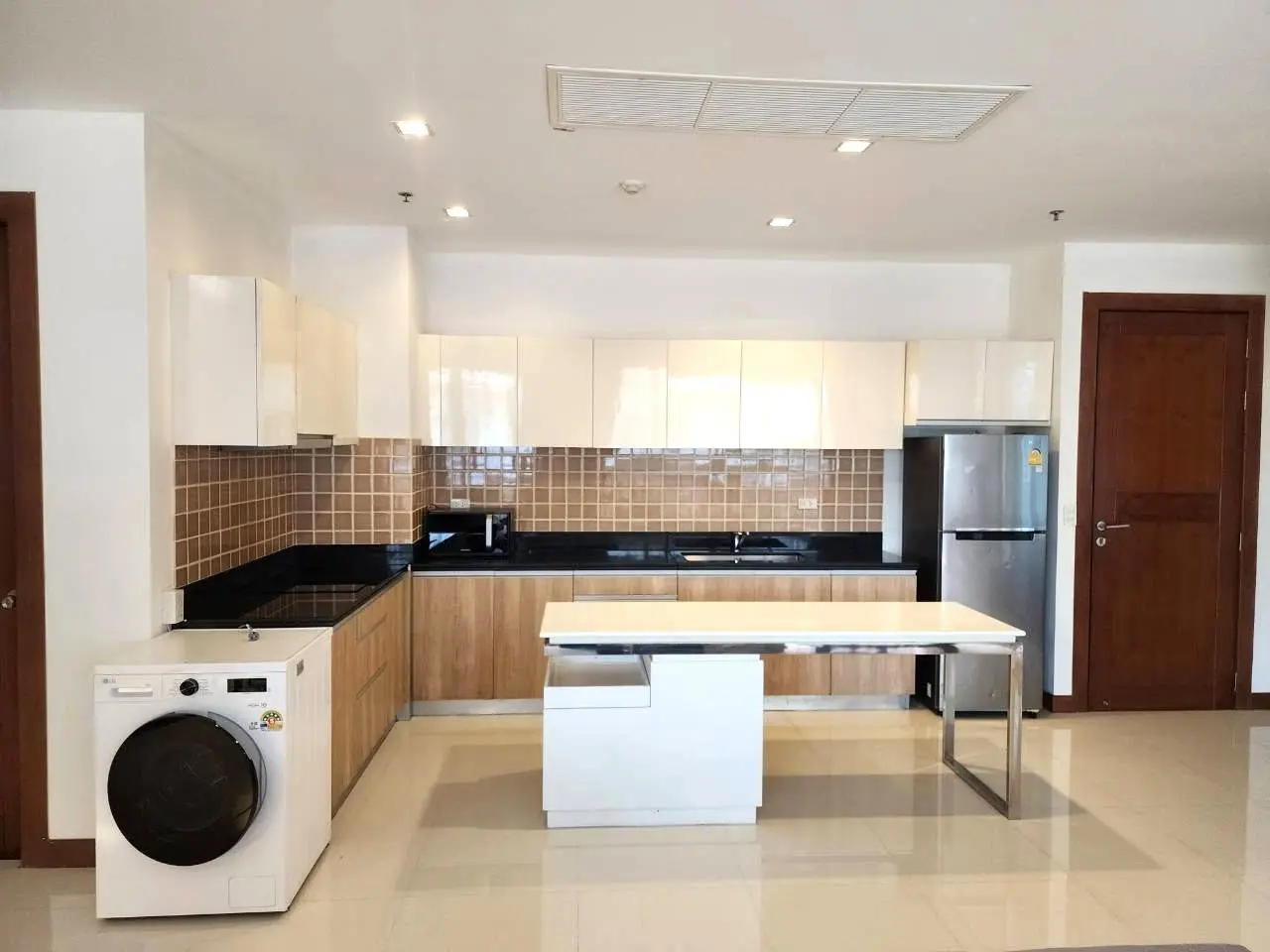 Modern open kitchen with glossy white cabinets and black granite countertops in a 2-bed condo for Pattaya City Resort