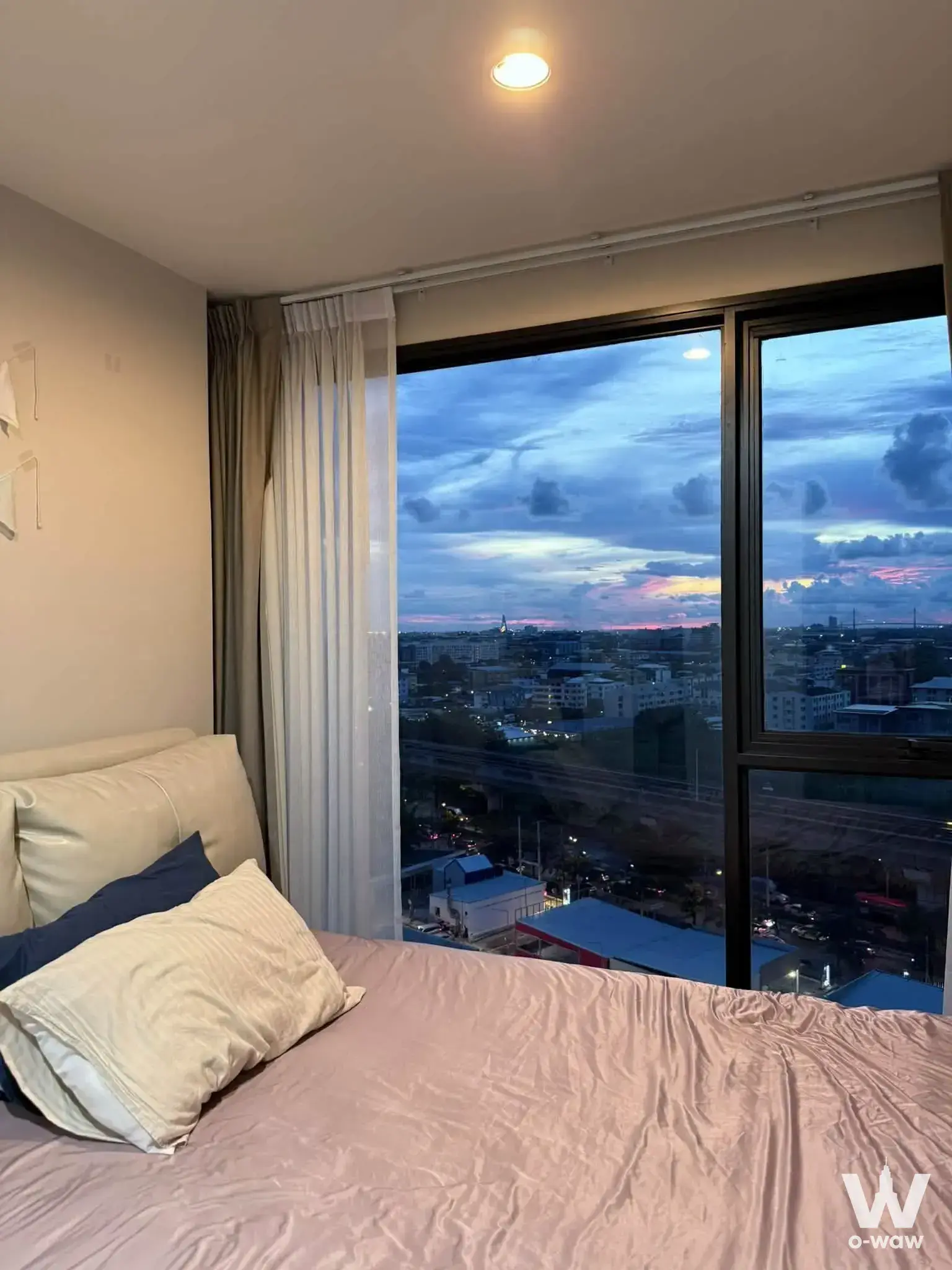 High-floor bedroom in Ideo Mobi Sukhumvit Eastpoint featuring city skyline view at dusk and cream upholstered bed