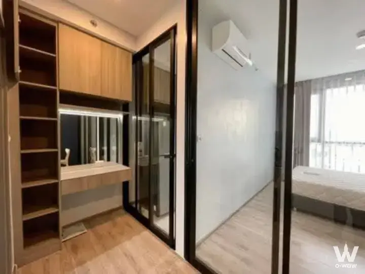 Bedroom with grey linens visible through glass doors next to a modern vanity with white countertops