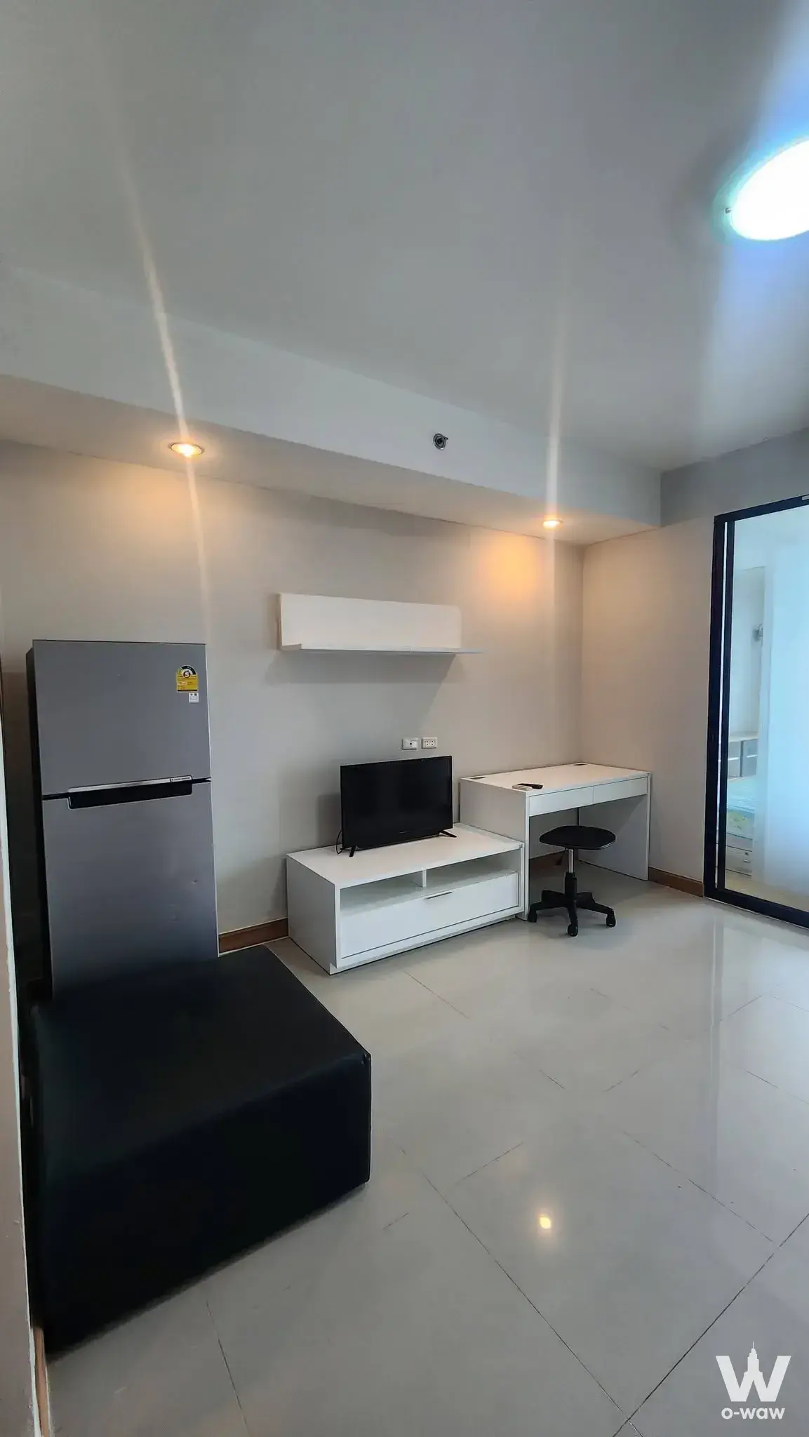 Sparsely furnished studio in Supalai Casa Riva Vista 1 with white walls, grey tile floor, and flat-screen TV