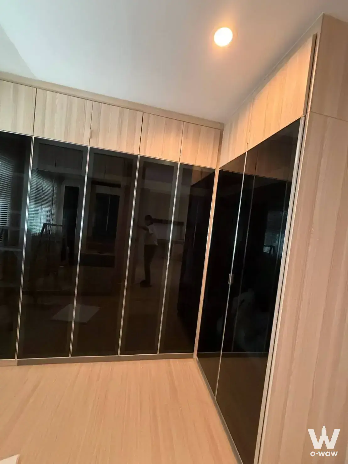 Walk-in closet with light oak ceiling-high cabinets and dark smoked glass sliding doors in a Nirvana Define Rama 9 condo
