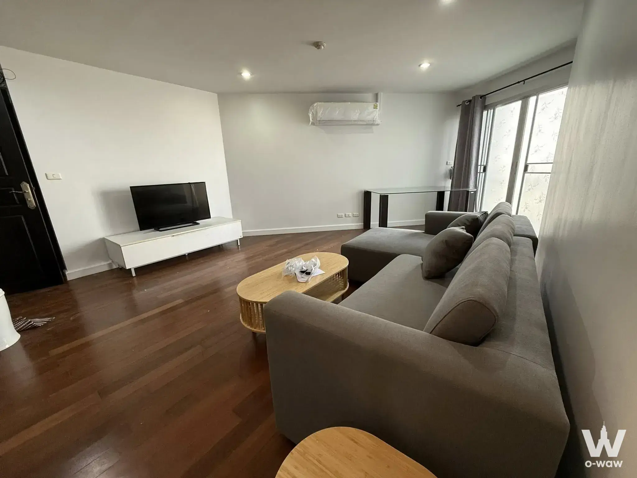 2-bed condo for rent in Belle Park Residence showing a living room with dark-brown wood flooring and a grey L-shaped