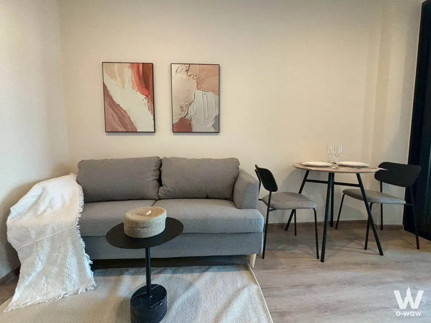 Living room in Nue District R9 condo featuring grey sofa, earth-tone art, and wooden dining set