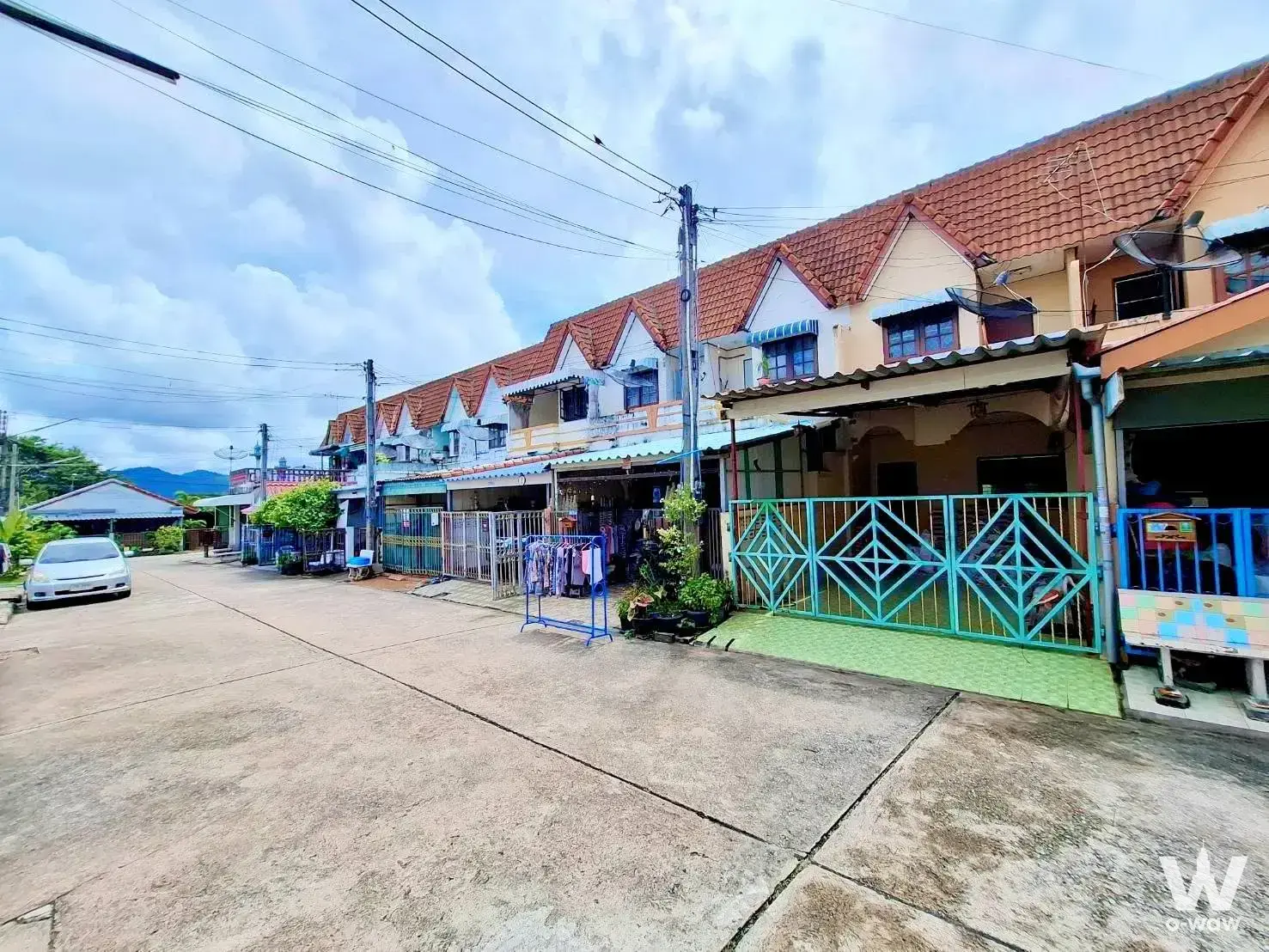 The street shows a 2-bed Ban Chan Condominium sale with terraced homes, red tile roofs and a teal gate