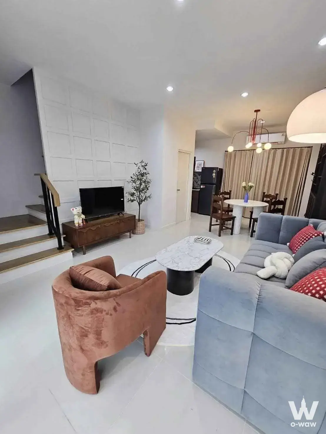 Open-plan living area with grey sectional sofa and wooden staircase, 3-bed townhouse for rent in Baan Klang Muang Rama 9