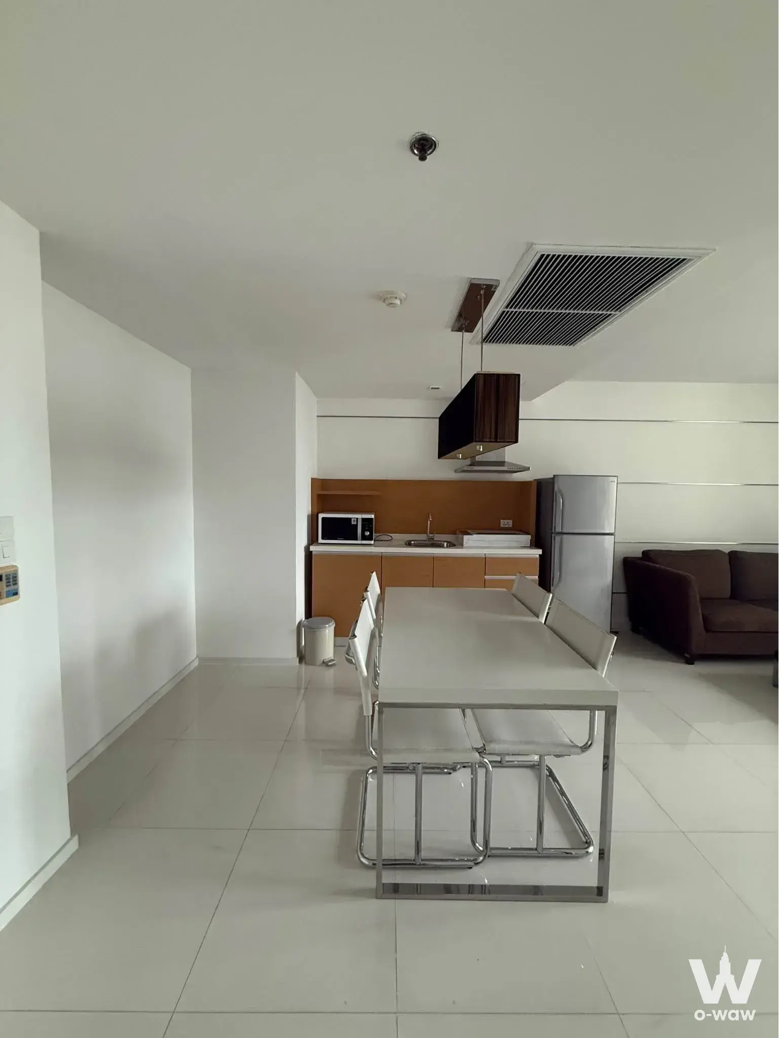 Open-plan living and dining area in Sathorn Prime Residence condo with white tiles, pendant light, and kitchenette