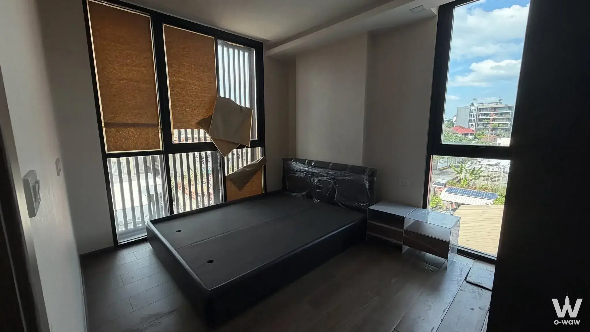 Sparsely furnished bedroom with dark wood floors, black bed frame, and city view from The Remarkable Soonvijai Soi 2 condo
