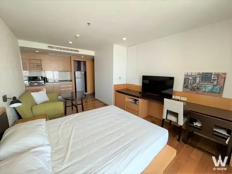 Open-plan studio bedroom with built-in desk and light wood cabinetry in Sathorn Prime Residence
