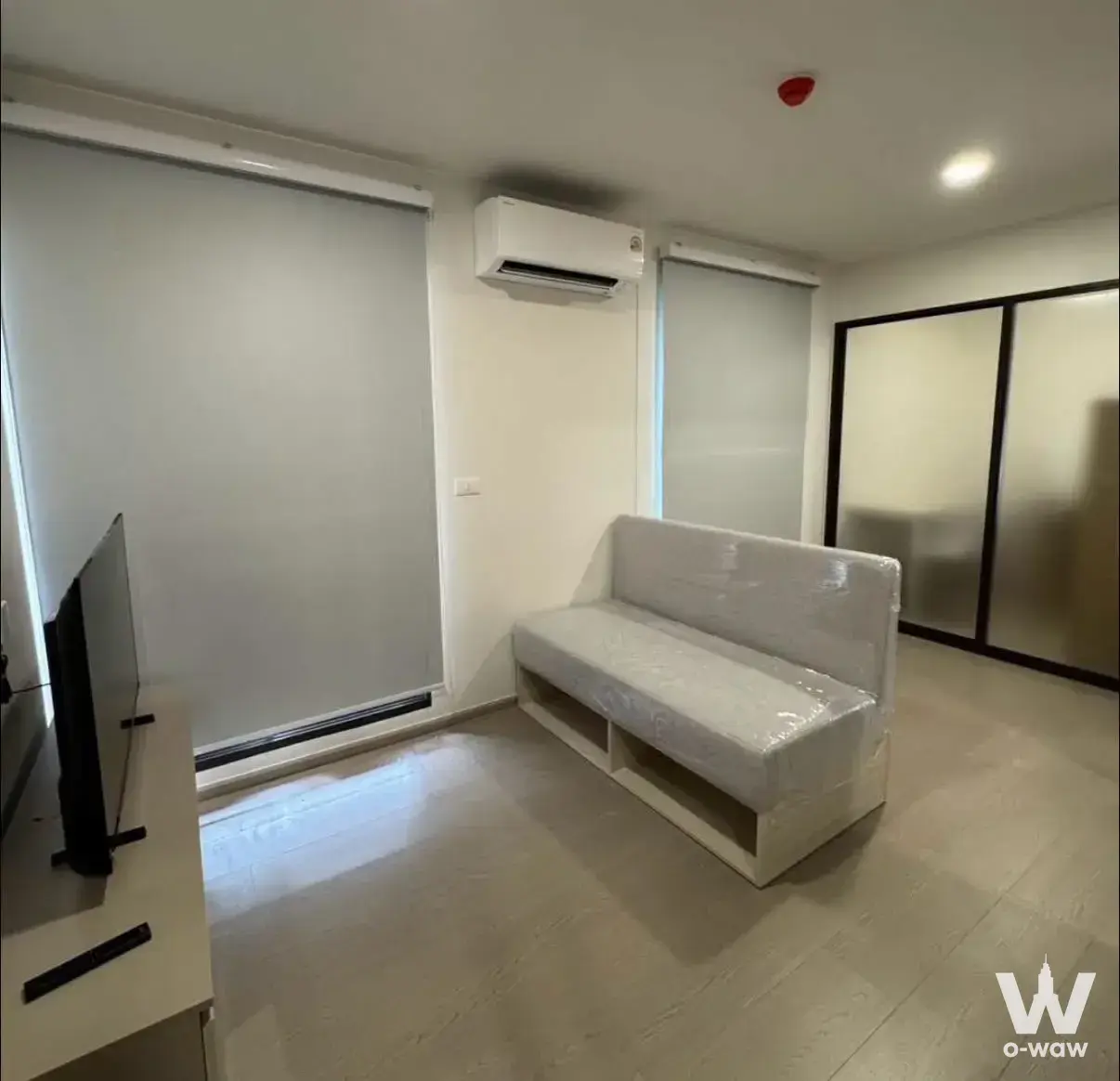 The 1-bed condo for rent in GOOD DAY Sukhumvit 93 has a living room with a frosted glass partition and plastic-wrapped sofa