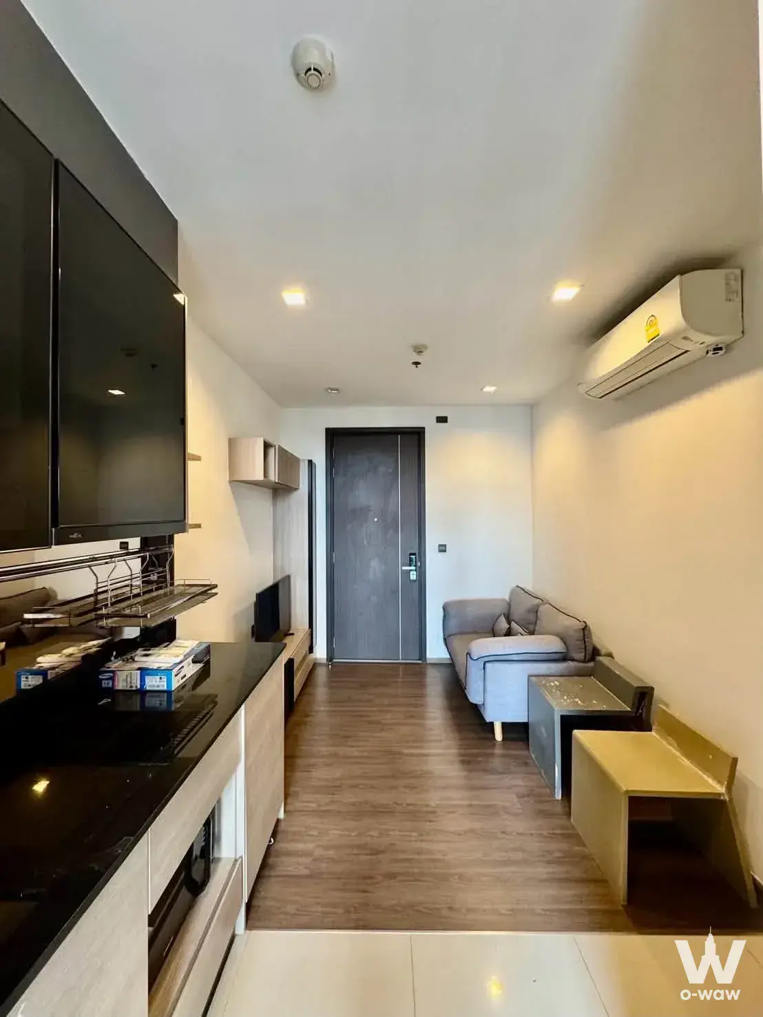 Open-plan living room with grey sofa and black granite island in this 1-bed condo for rent at THE LINE Asoke-Ratchada