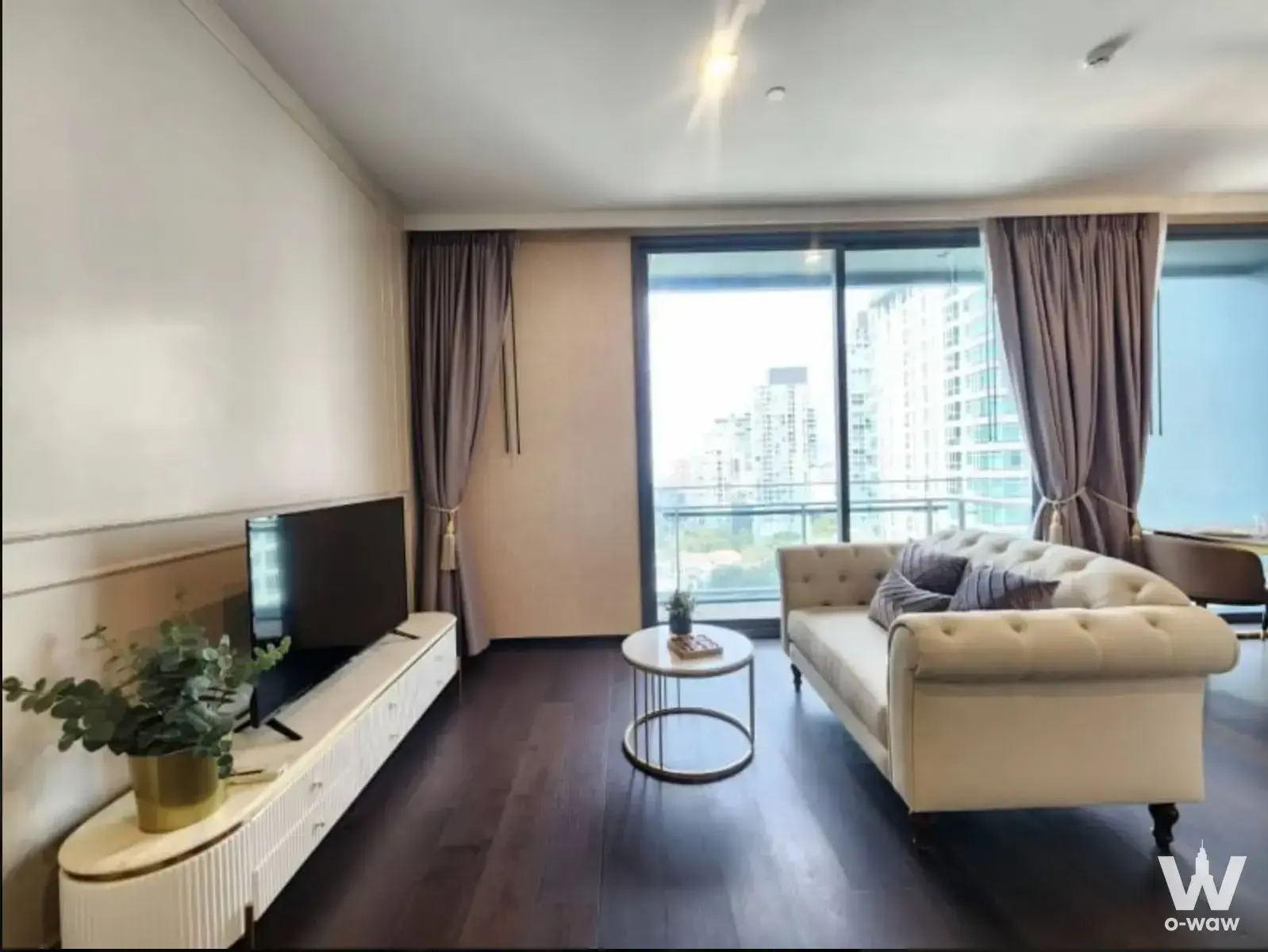 LAVIQ Sukhumvit 57 living room with cream Chesterfield sofa, marble coffee table, and city skyline view