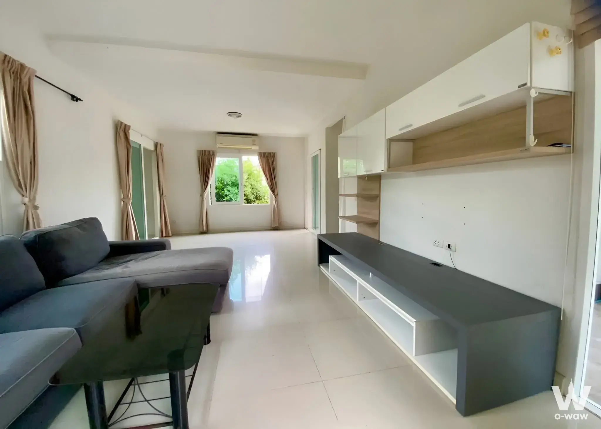 The living room in a 4-bed house for rent at Kanasiri Wongwaen-Rama 5 has a grey sectional sofa and green foliage views