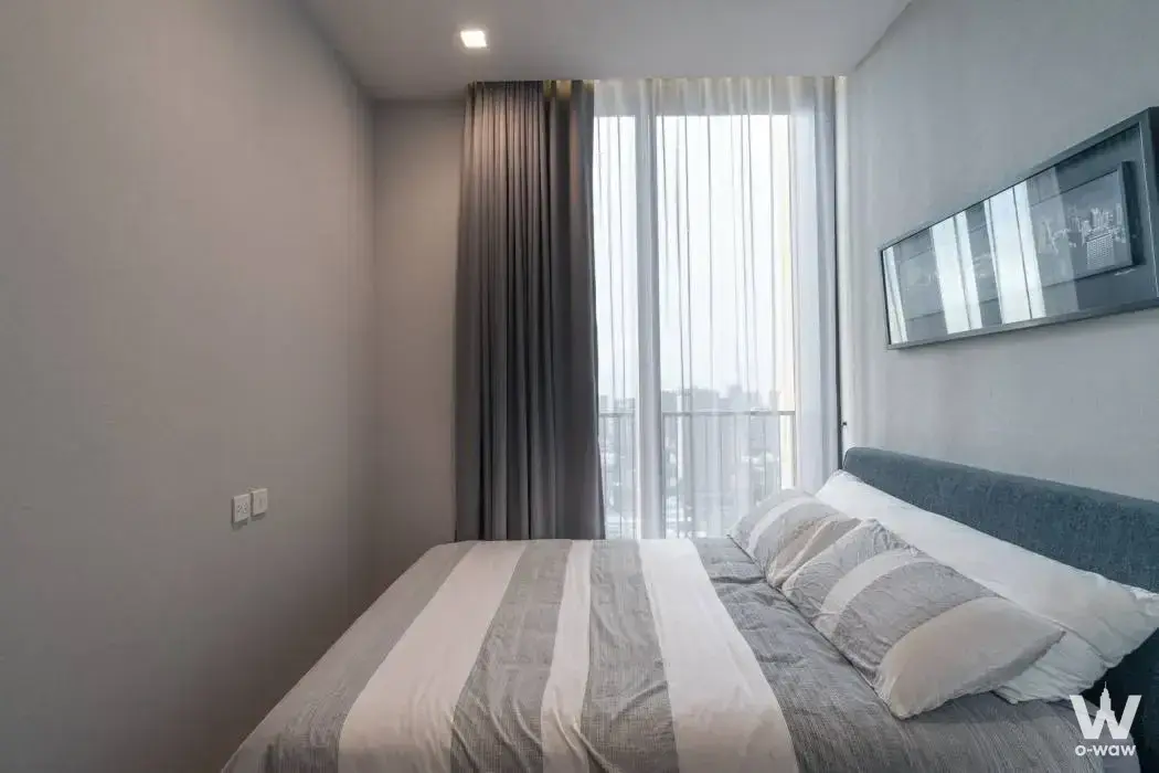 Noble BE19 2-bed condo bedroom with striped duvet and city skyline view