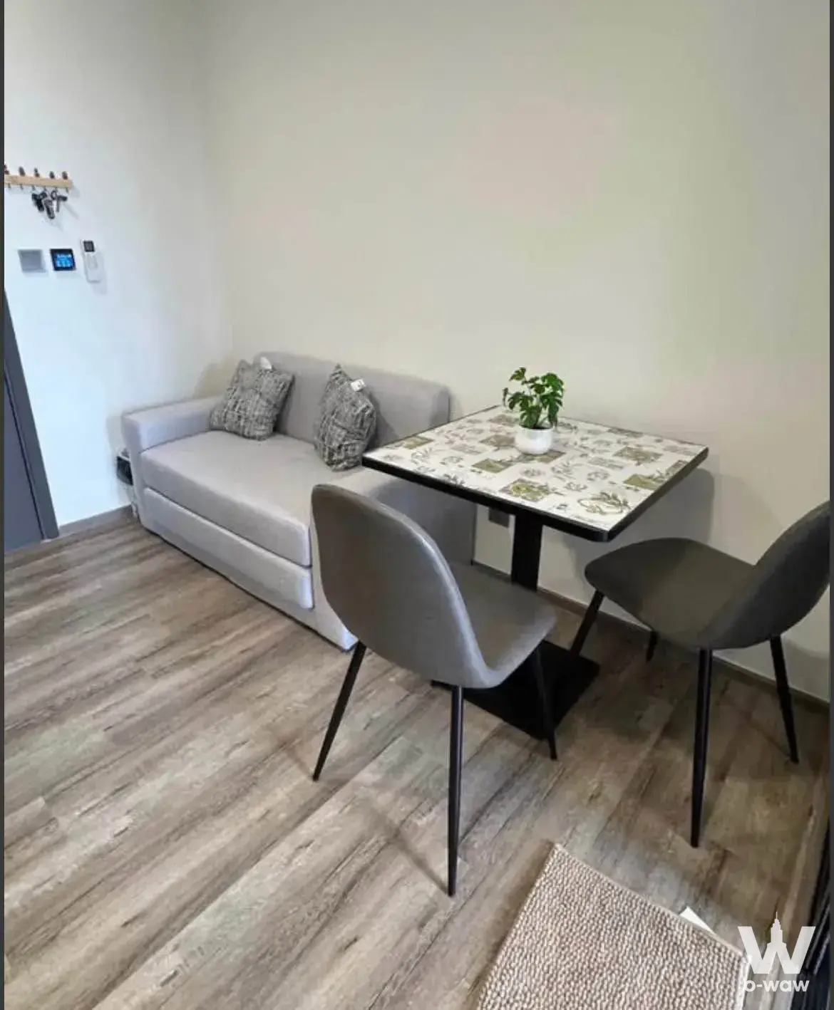 Compact living area in Modiz Vault Kaset Sripatum with grey sofa, botanical print table, and minimalist decor