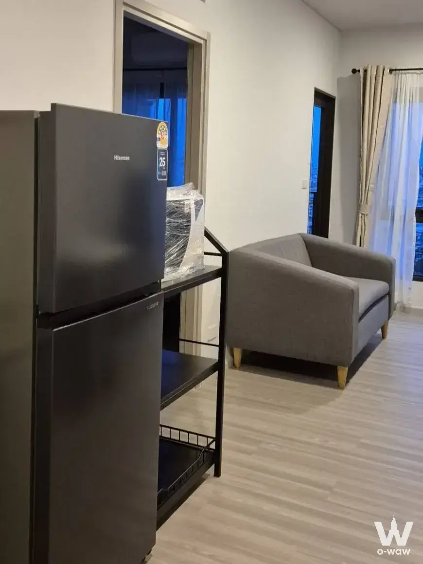 Furnished living room in a QUINTARA MHy'DEN PHO NIMIT 1-bed rental featuring a grey loveseat and matte-black refrigerator