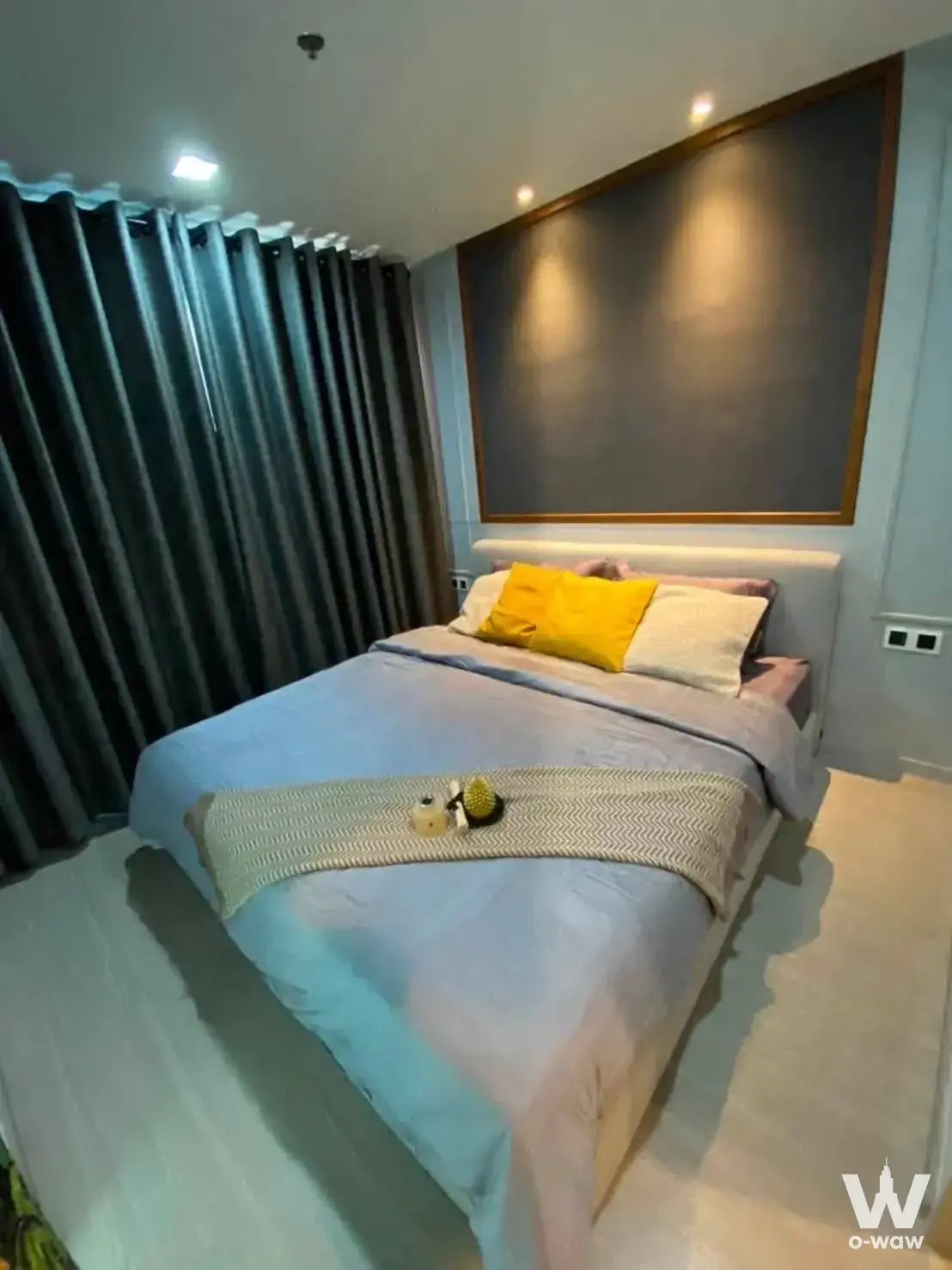 Modern bedroom in Life Ladprao 1-bed condo with grey headboard, blue duvet, and yellow accent pillow
