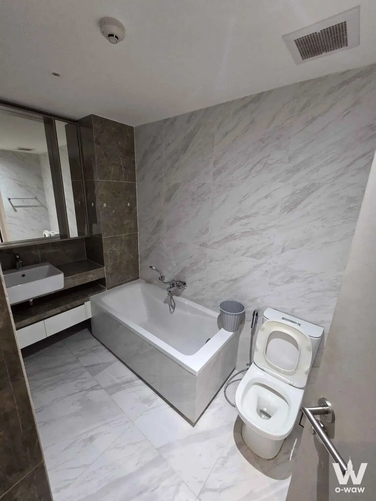 The bathroom has marble-look tiles, a vessel sink, a bathtub and a toilet in a 1-bed Fynn Asoke condo
