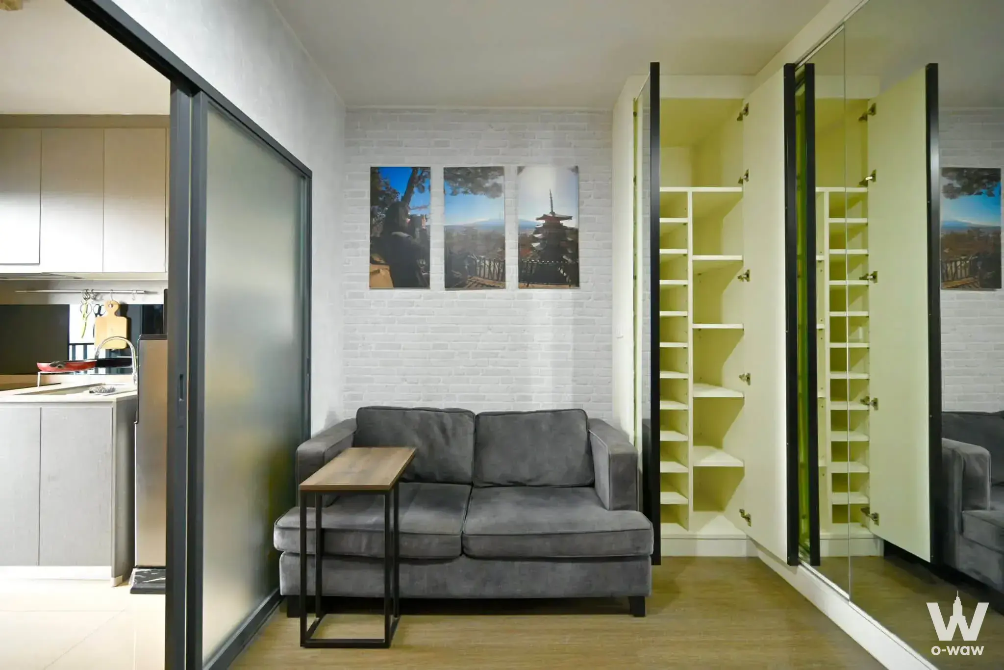Ideo Sukhumvit 93 1-bed living room with grey sofa, faux-brick wall art, mirrored wardrobe, and frosted glass partition