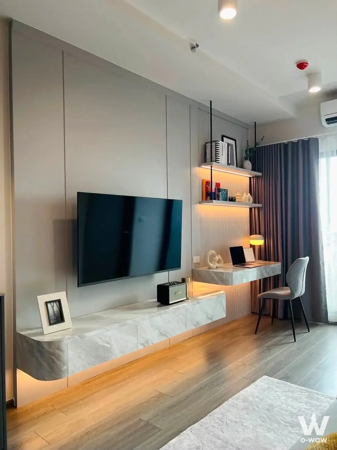 Living room with grey wall paneling, marble media console, and desk area in this IdeO Sukhumvit Rama 4 condo