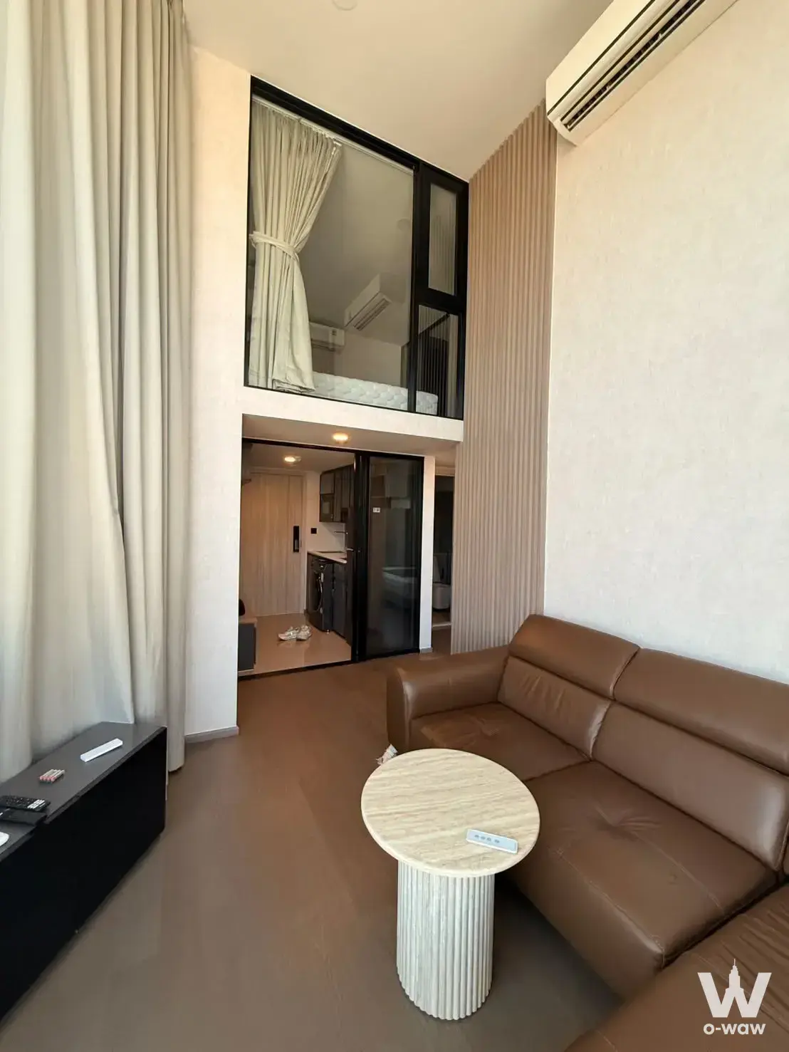 Duplex living room in Park Origin Chula-Samyan with double-height ceiling, mezzanine, and brown leather sofa