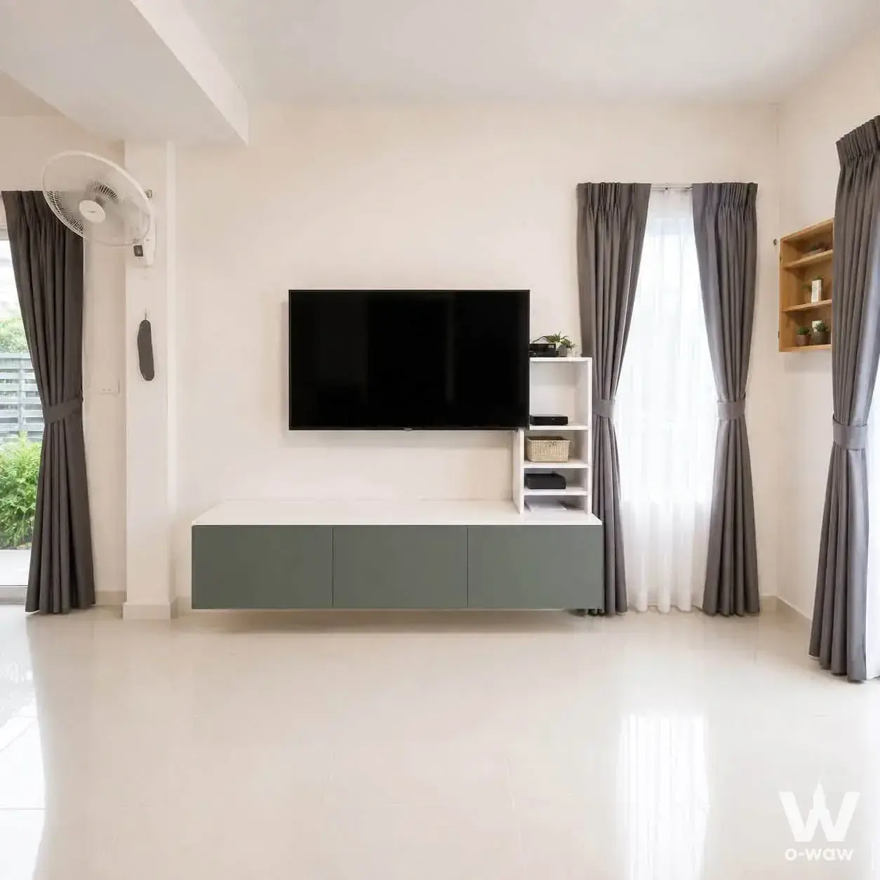 The living room in a 3-bed Villaggio Bangna townhouse has a wall-mounted TV, white shelving and a glossy white tile floor