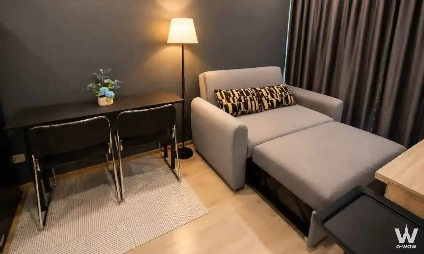 Ideo Wutthakat 1-bed condo living room with charcoal walls, light wood floors, and a grey chaise lounge