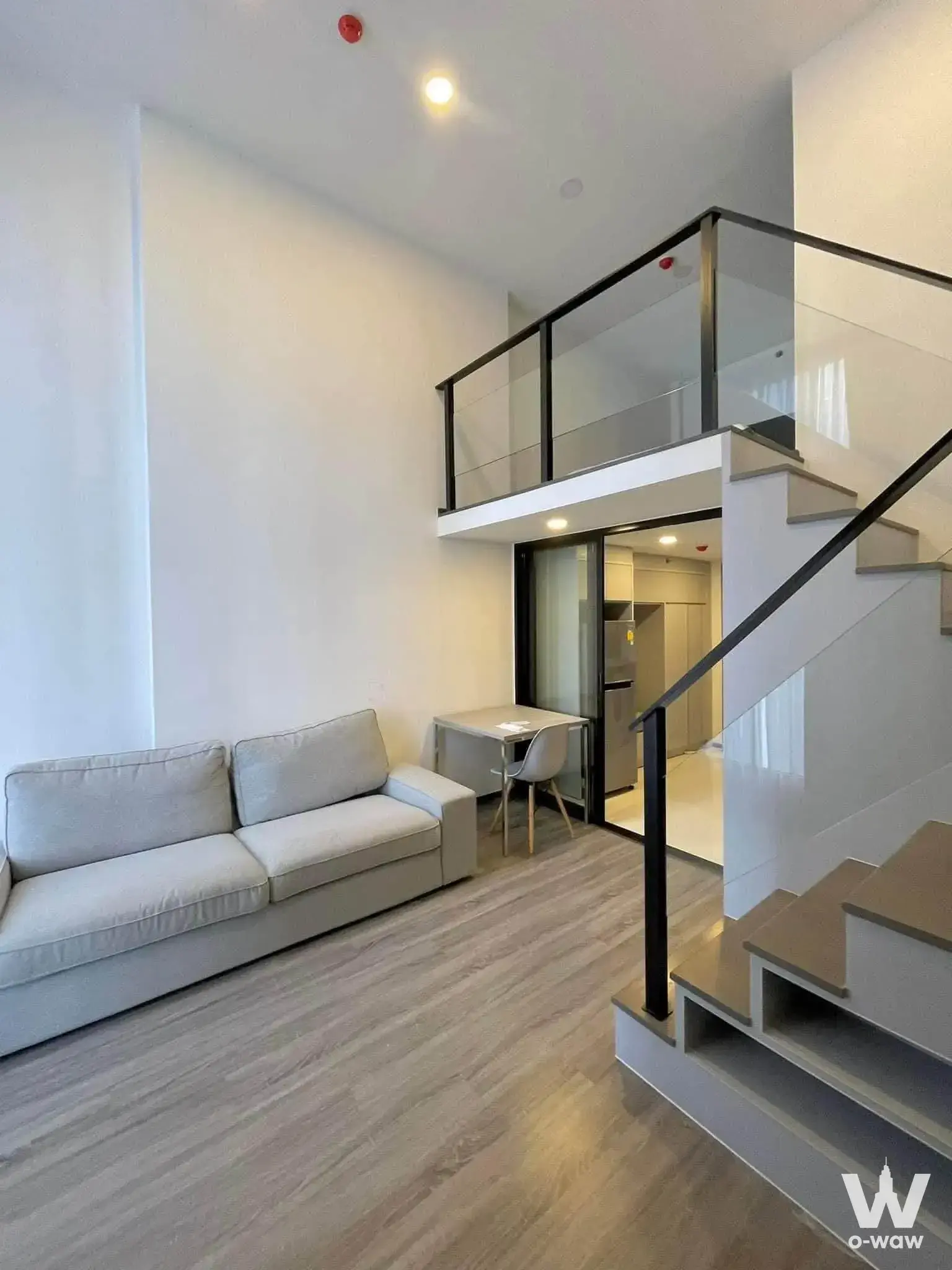Loft living room in KnightsBridge Space Ratchayothin with grey sofa, open staircase, and mezzanine level