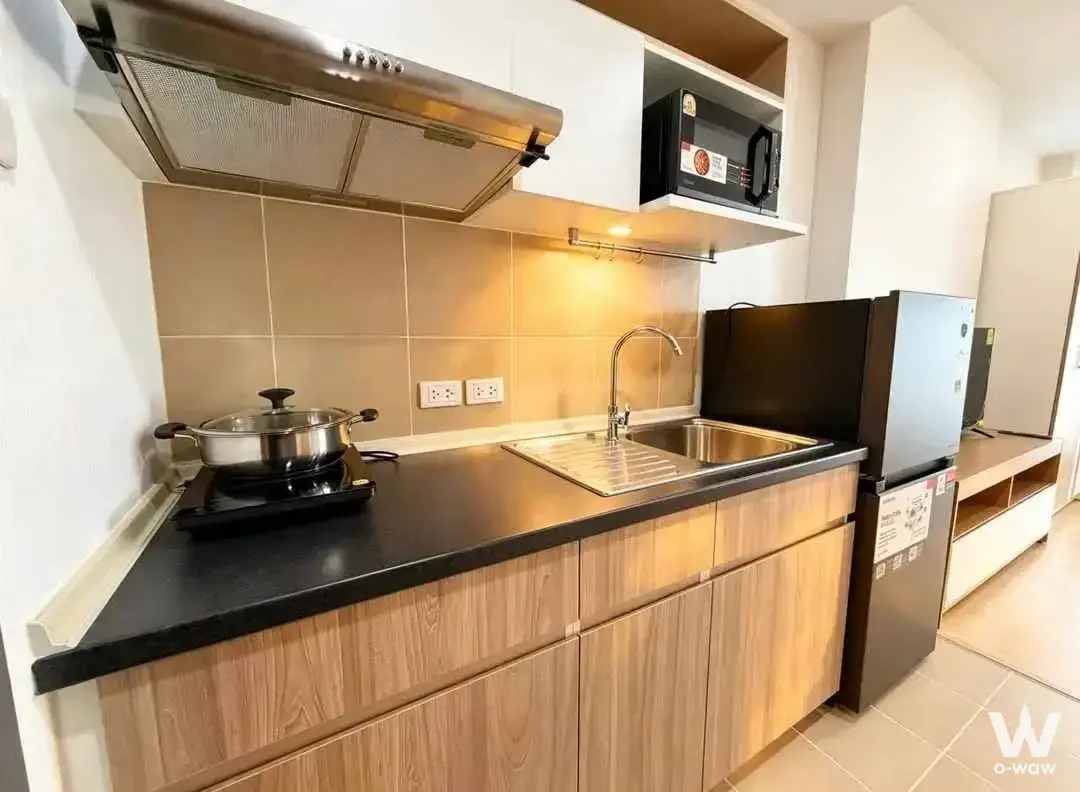 Compact kitchenette in Supalai Veranda Ramkhamhaeng with light wood cabinets and black laminate countertops