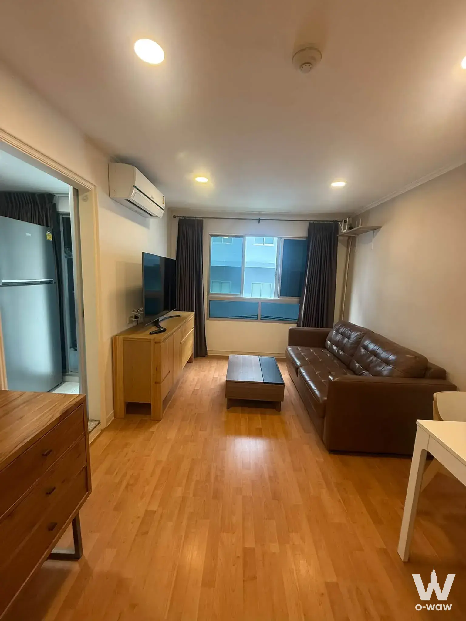Lumpini Ville Cultural Center 1-bed condo living room with wood-look laminate floor and brown leather sofa