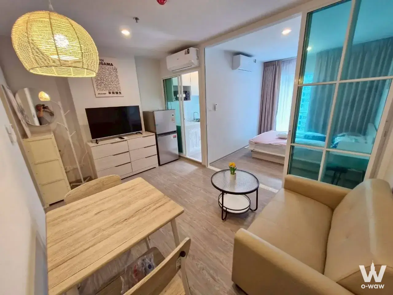 Furnished studio in Regent Home Bangna featuring light wood floors, beige sofa, and open kitchenette