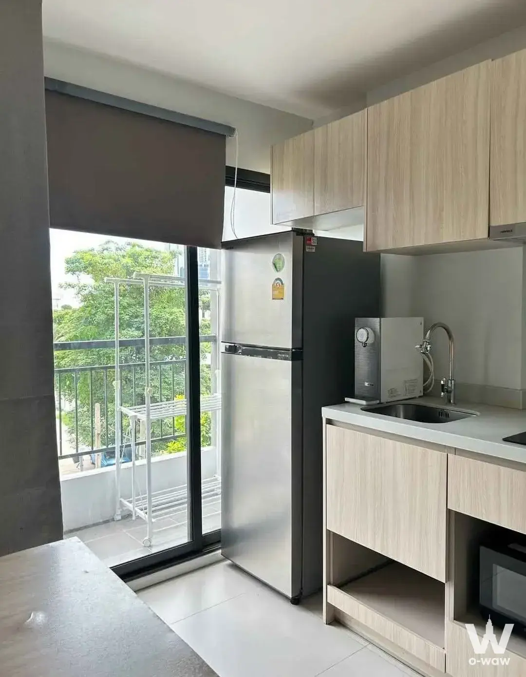 Compact kitchenette with light wood cabinetry and balcony access in a 1-bed unit for rent at The Nest Sukhumvit 64