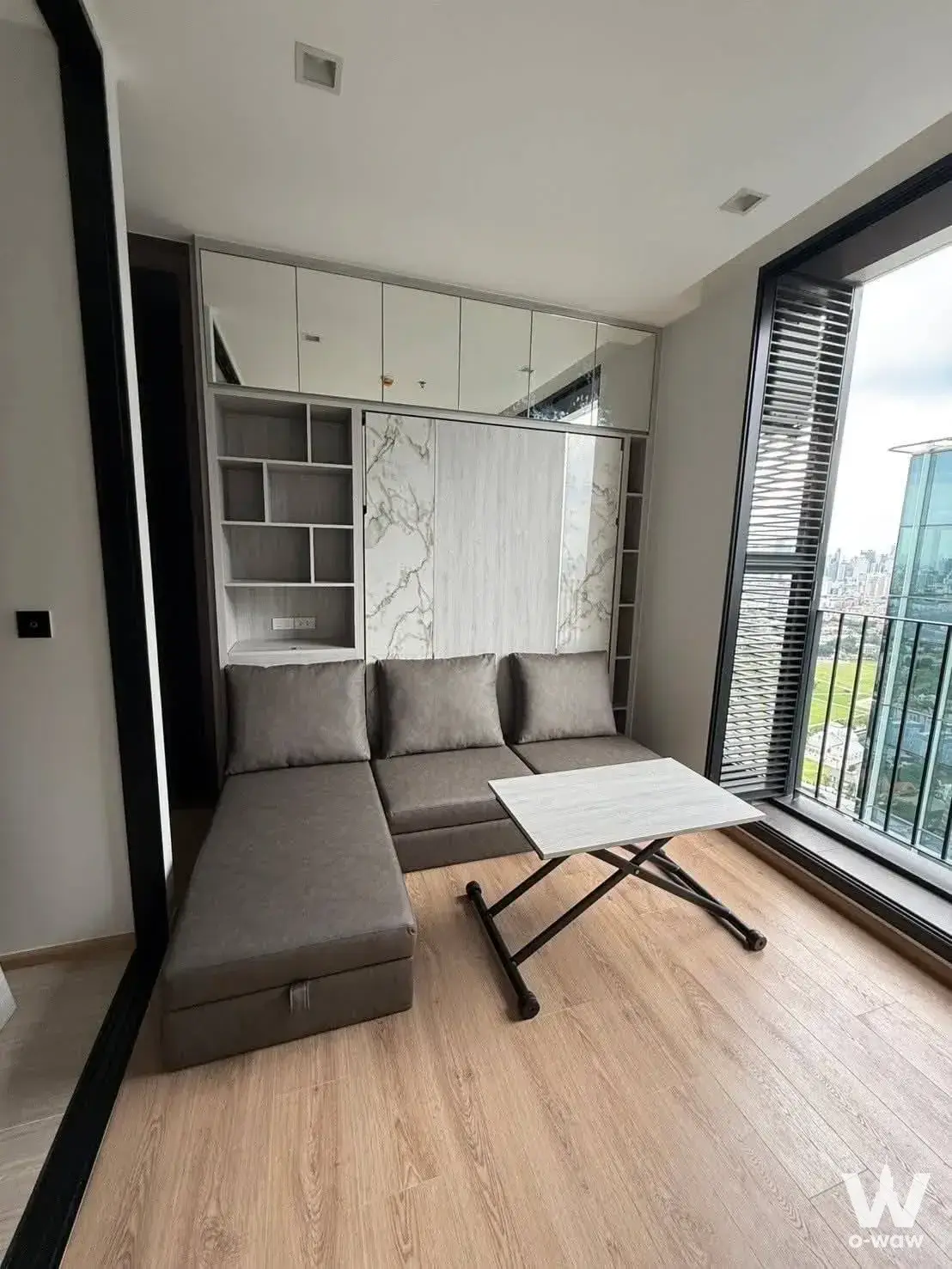 Noble Around Ari 1-bed condo living room featuring L-shaped sofa and city skyline view