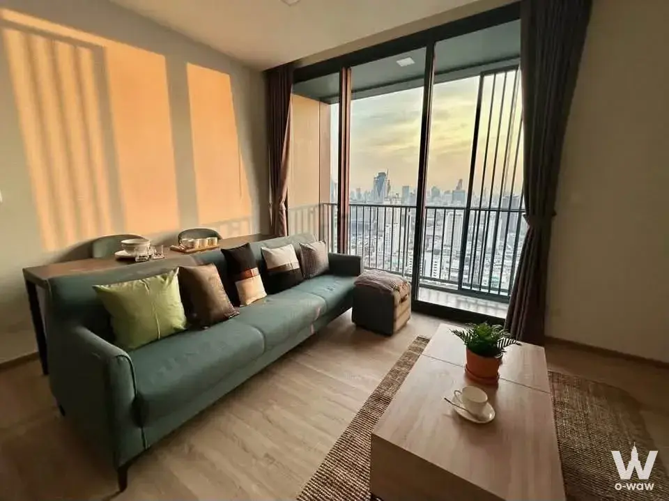 2-bed condo for rent in XT Phayathai living room with teal sofa and sunset city skyline view