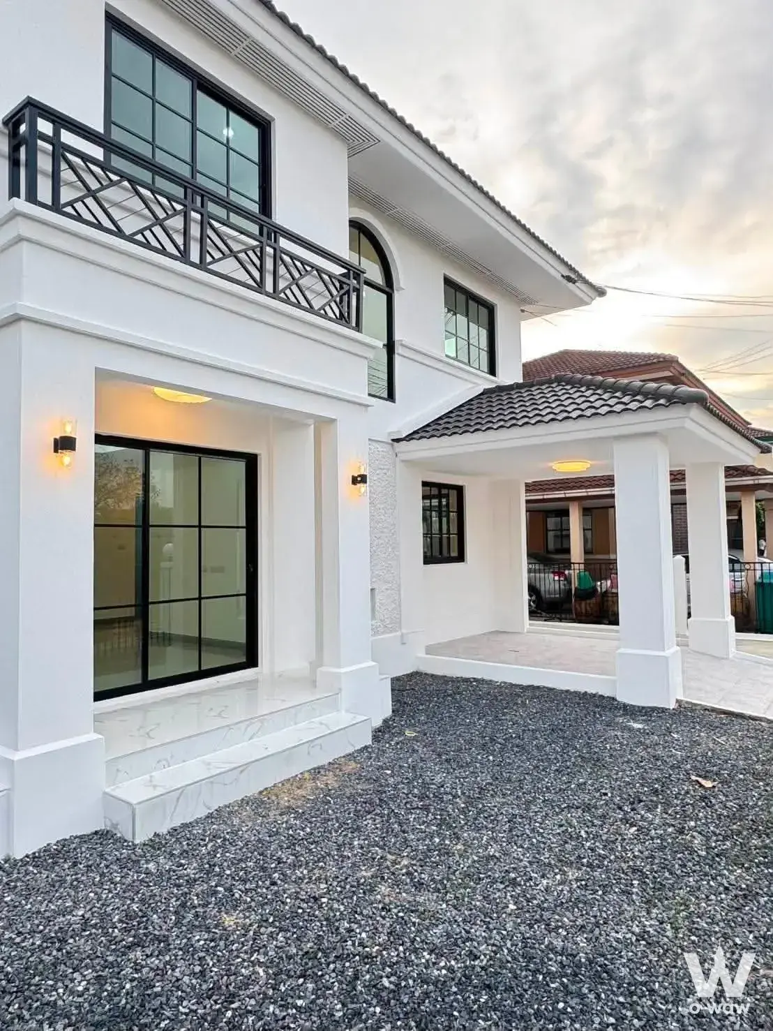 White two-story house for sale in มัณฑนา 2 ศรีนครินทร์ has black grid windows and a covered carport