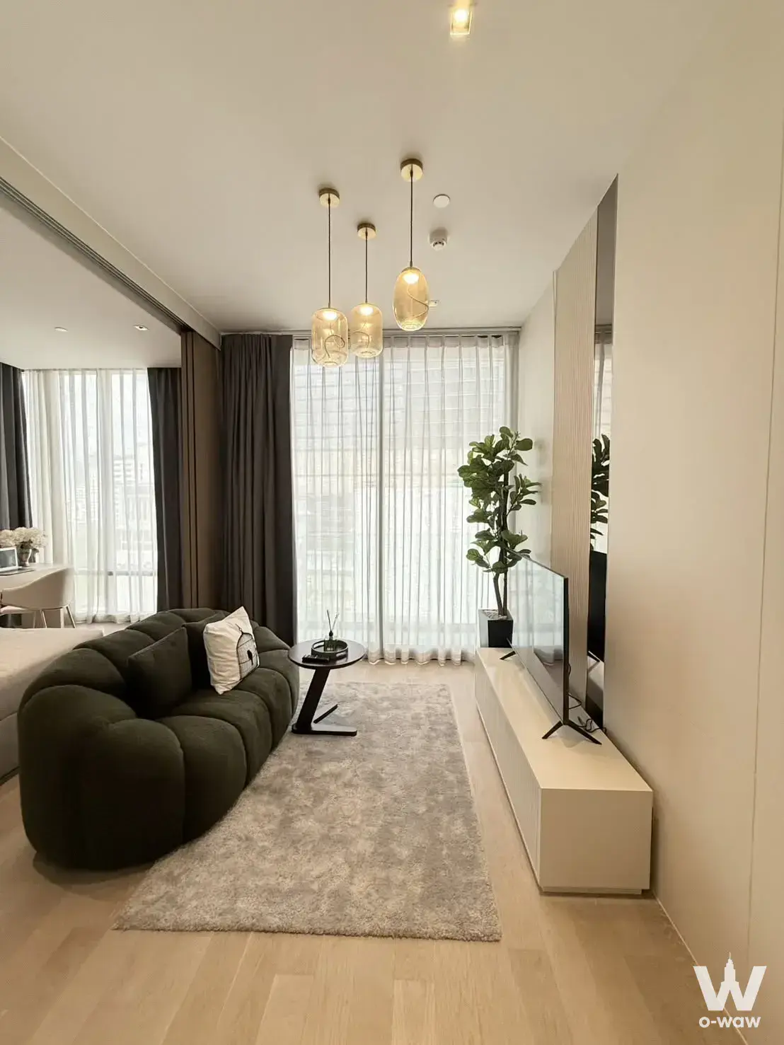 Living room in an Ashton Silom condo showcasing an olive-green curved sofa and floor-to-ceiling windows