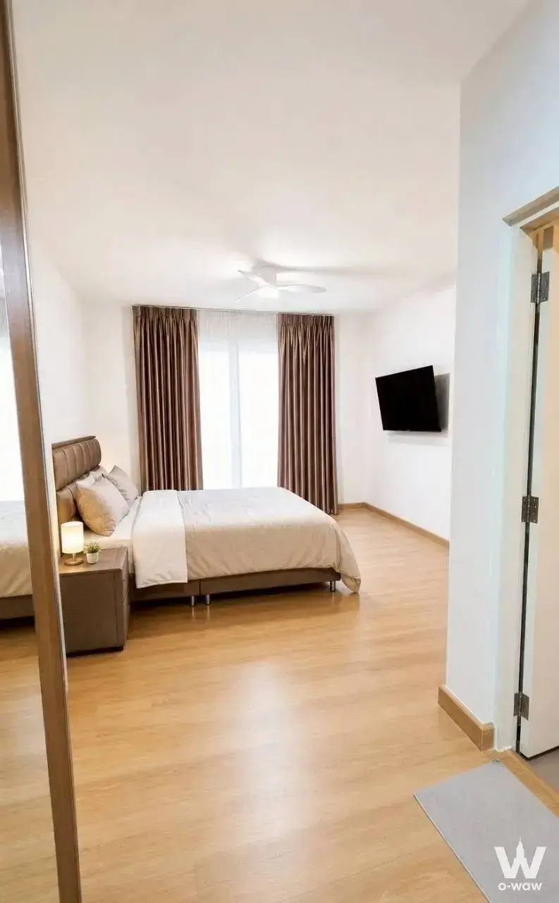 Master bedroom in Grande Pleno Mega Bangna house with brown upholstered bed and floor-to-ceiling drapes