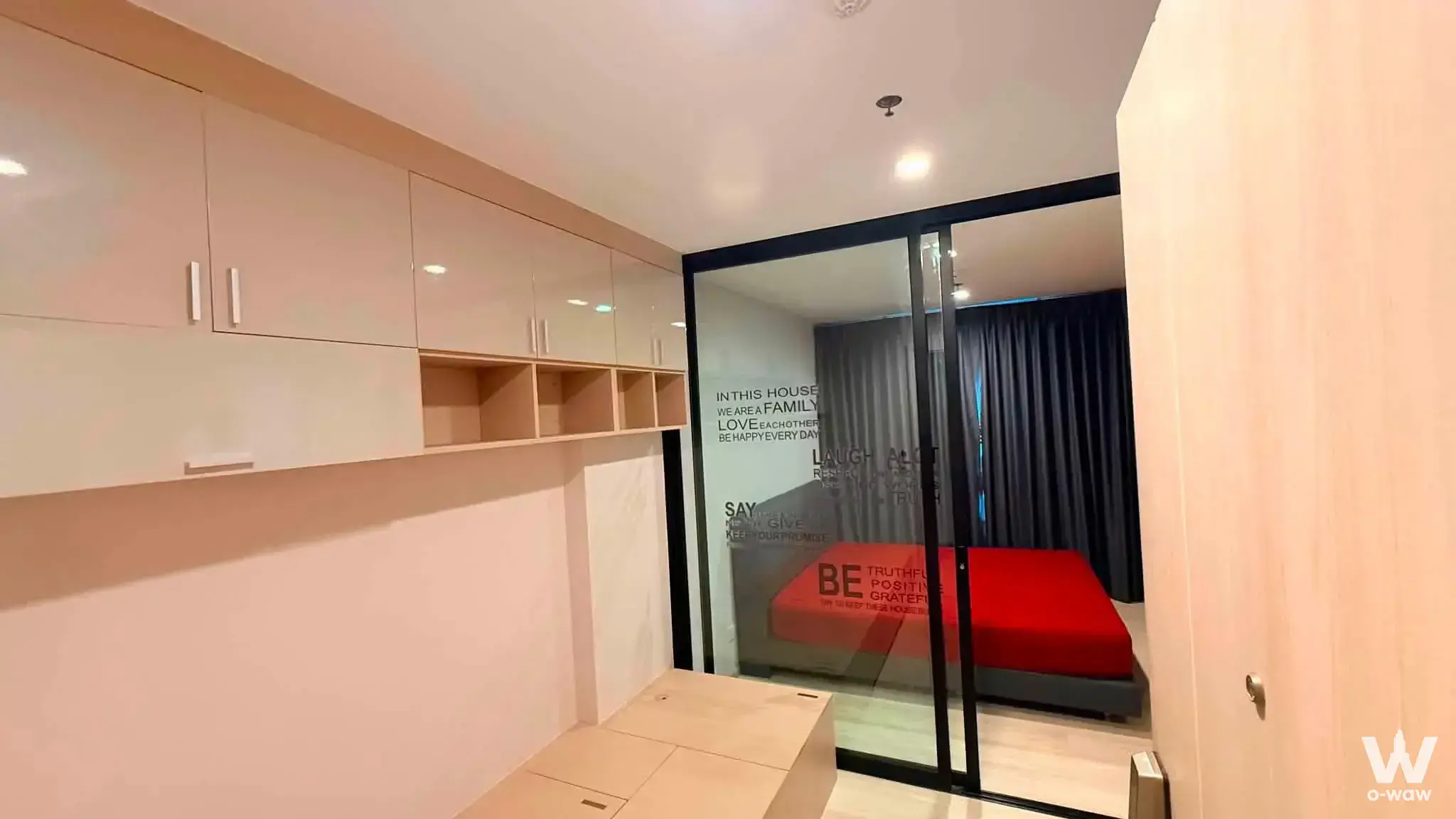 Studio entry hallway in Life Asoke featuring built-in white storage and glass partition revealing red bedding