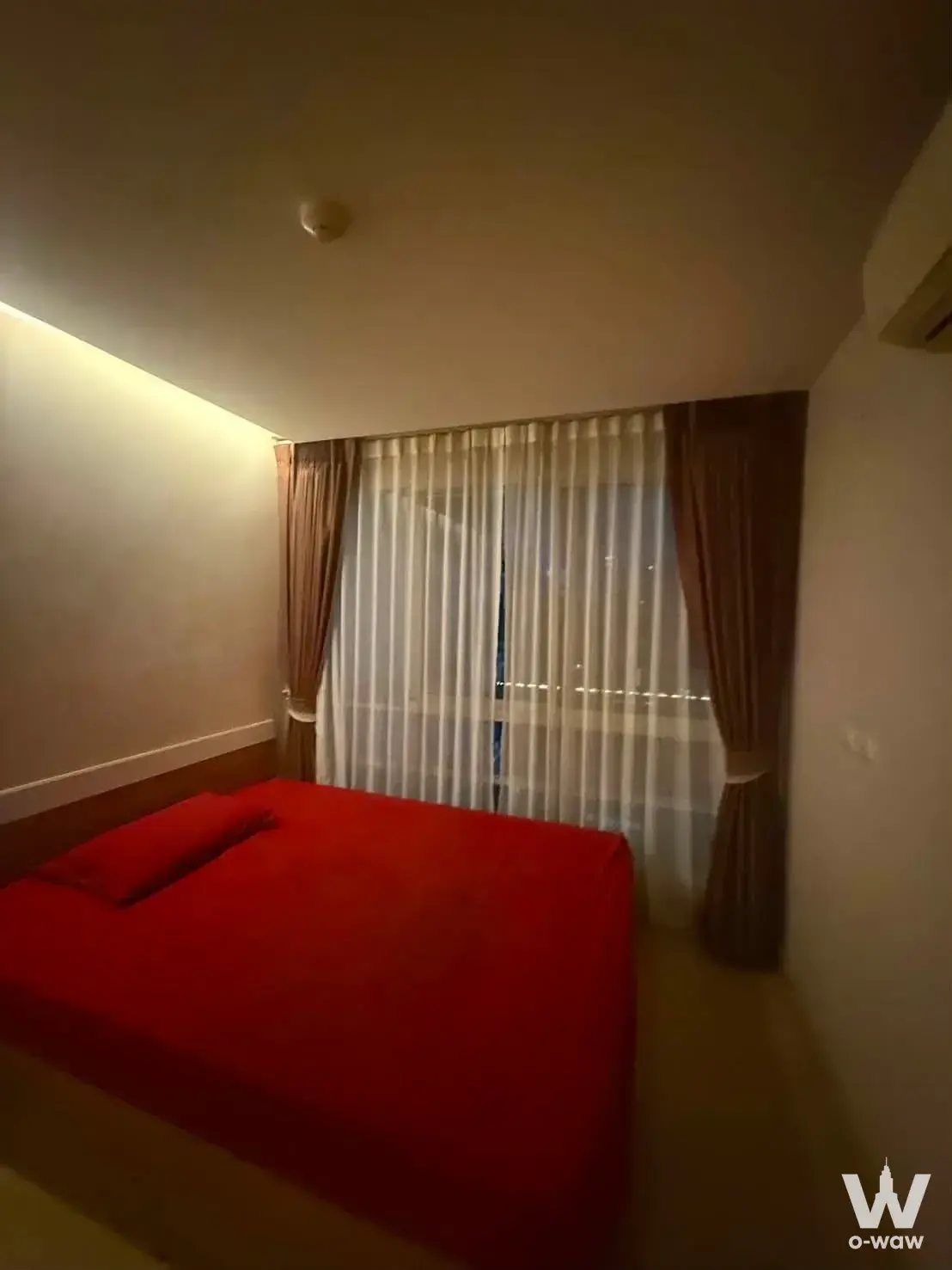 Queen bed with red linens in Emerald Residence Ratchada condo facing floor-to-ceiling window with city view
