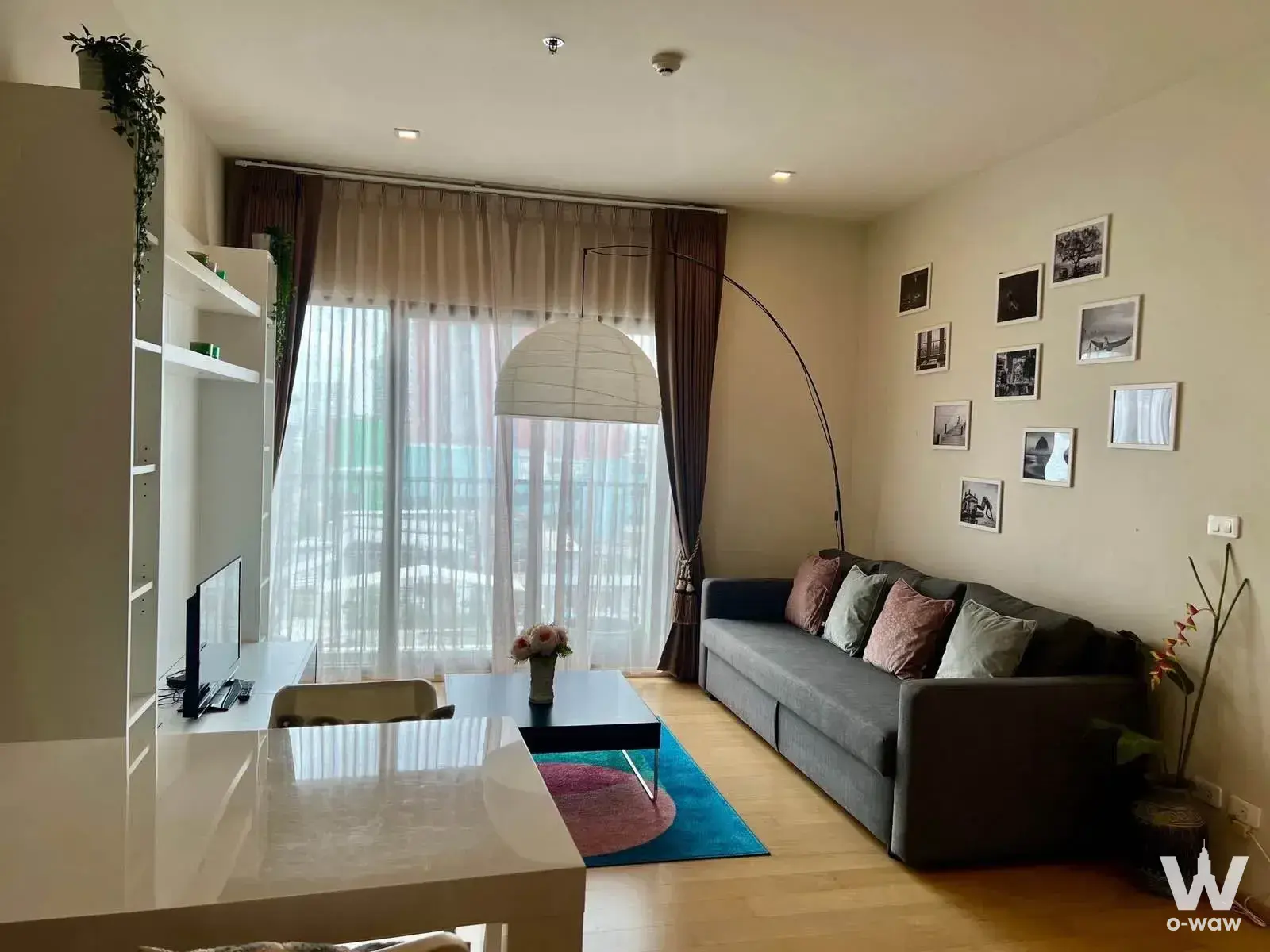 The living room in a 1-bed Noble Reform rental condo has a grey sofa, arched floor lamp and city-view window