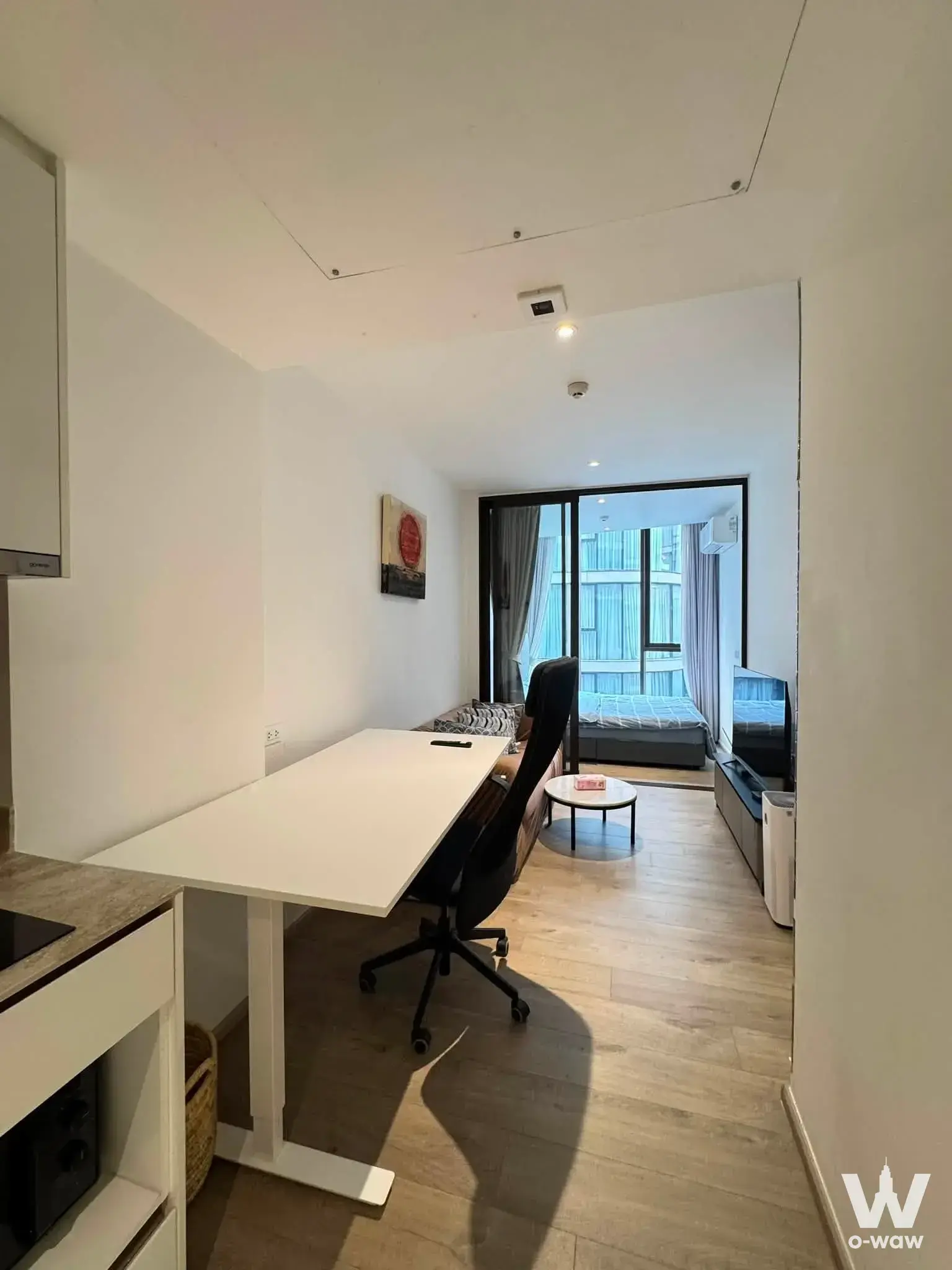 Open-plan studio in Fynn Asoke featuring a white desk, kitchenette, and queen bed under recessed lighting and wood floors