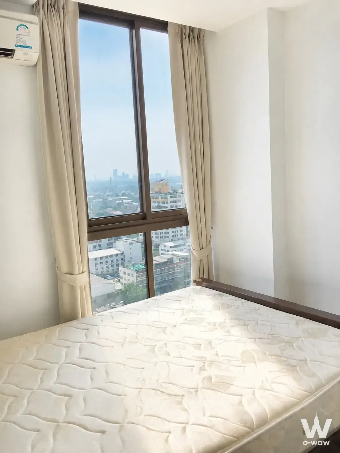 Minimalist bedroom featuring a low-profile bed and large sliding window with city views in a Sukhumvit 103 condo