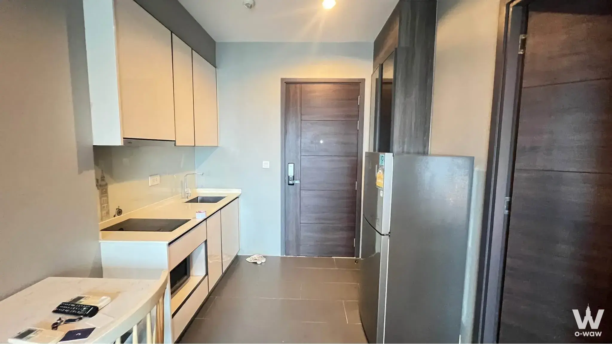 Compact kitchen in a 1-bed C Ekkamai Condominium with cream cabinets, black induction cooktop, and quartz counter