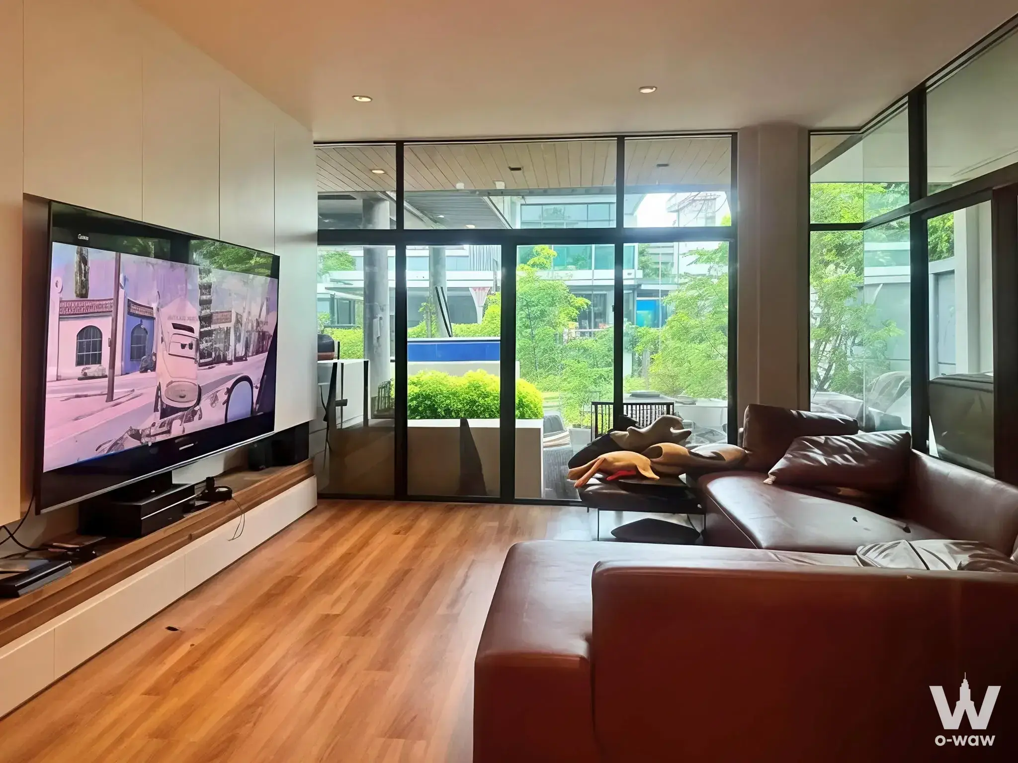 3-bed house for sale in Setthasiri Srinakarin featuring a minimalist living room with brown leather sofa and pool view