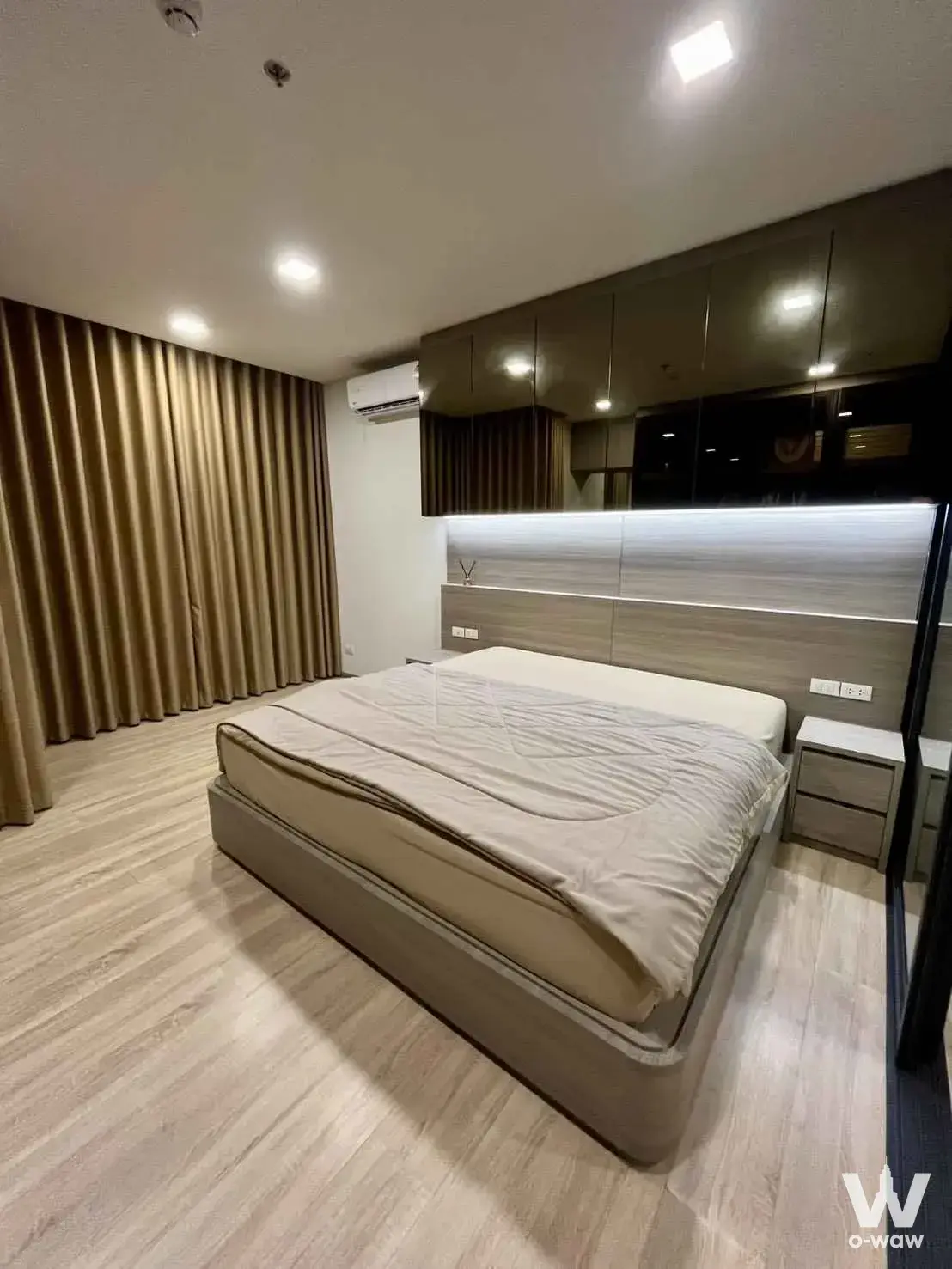 Master bedroom with a grey upholstered bed, built-in headboard with LED lighting, and gold-brown curtains in a 1-bed condo