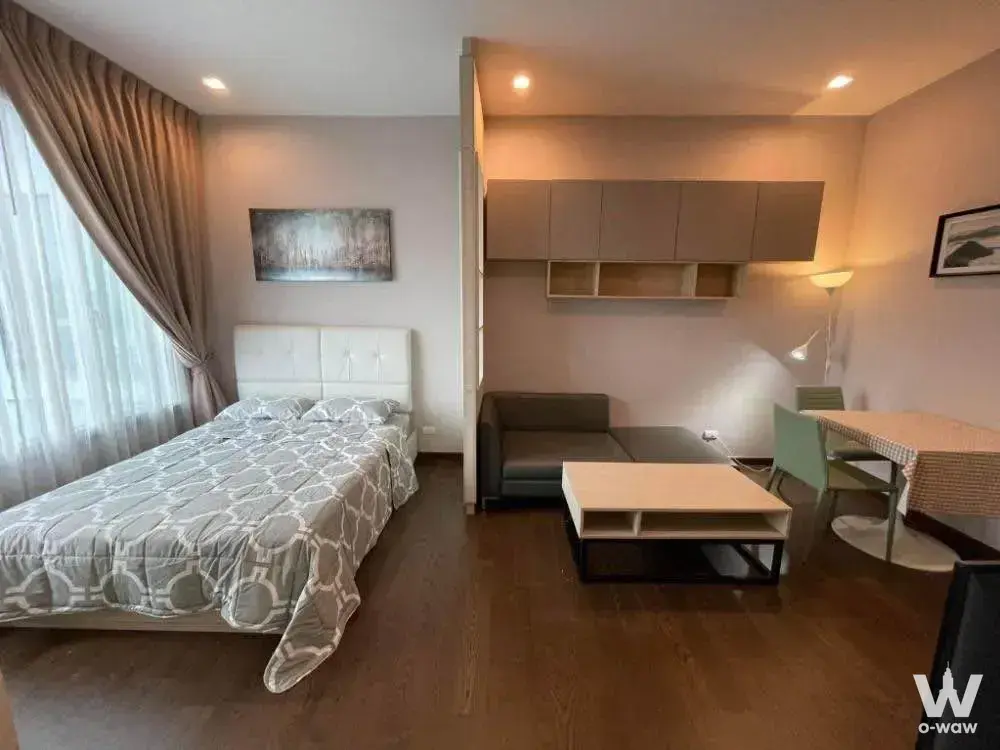 Q Asoke 1-bed condo studio with queen bed, leather sofa, and sage green dining chairs