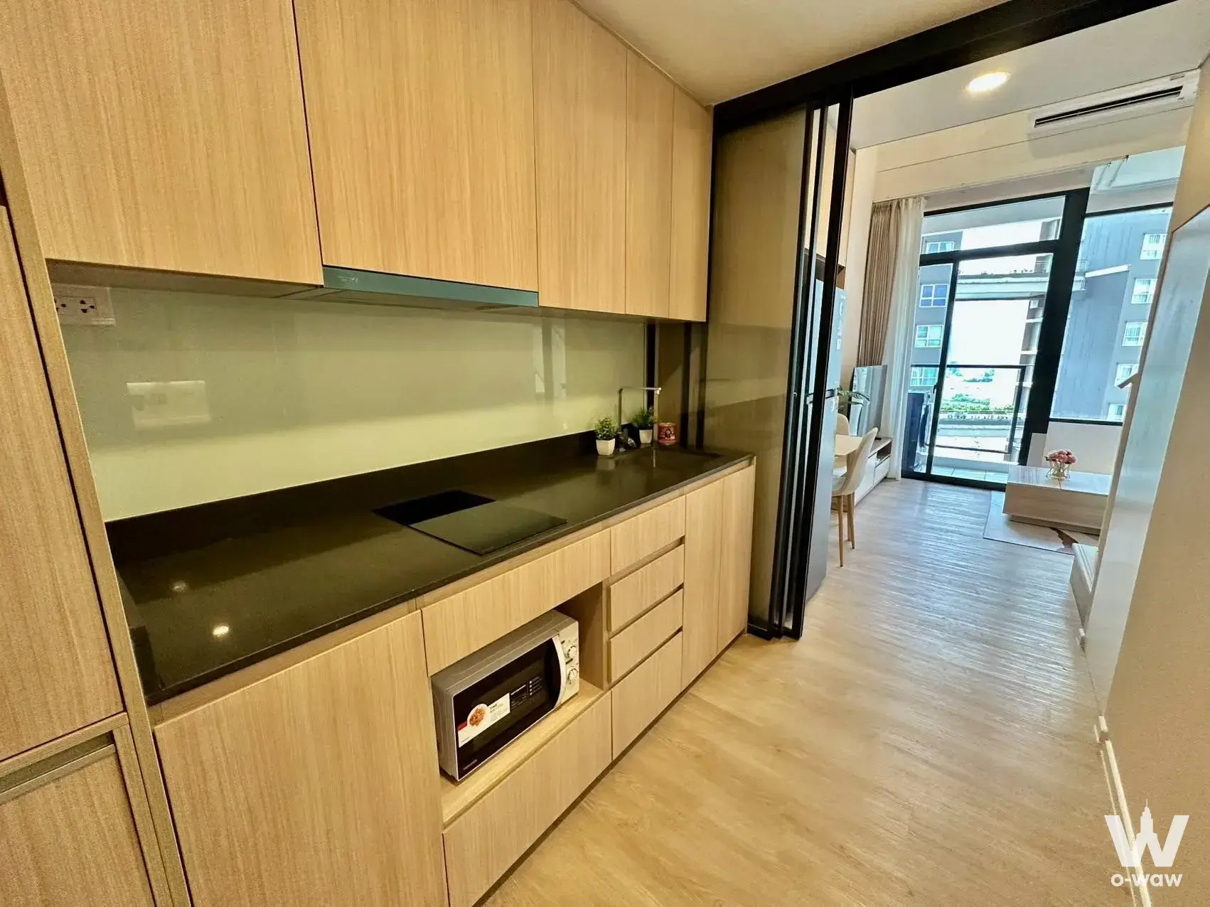 Open-plan kitchen with light wood cabinetry and black countertop in a 1-bed condo for rent at Siamese Residence
